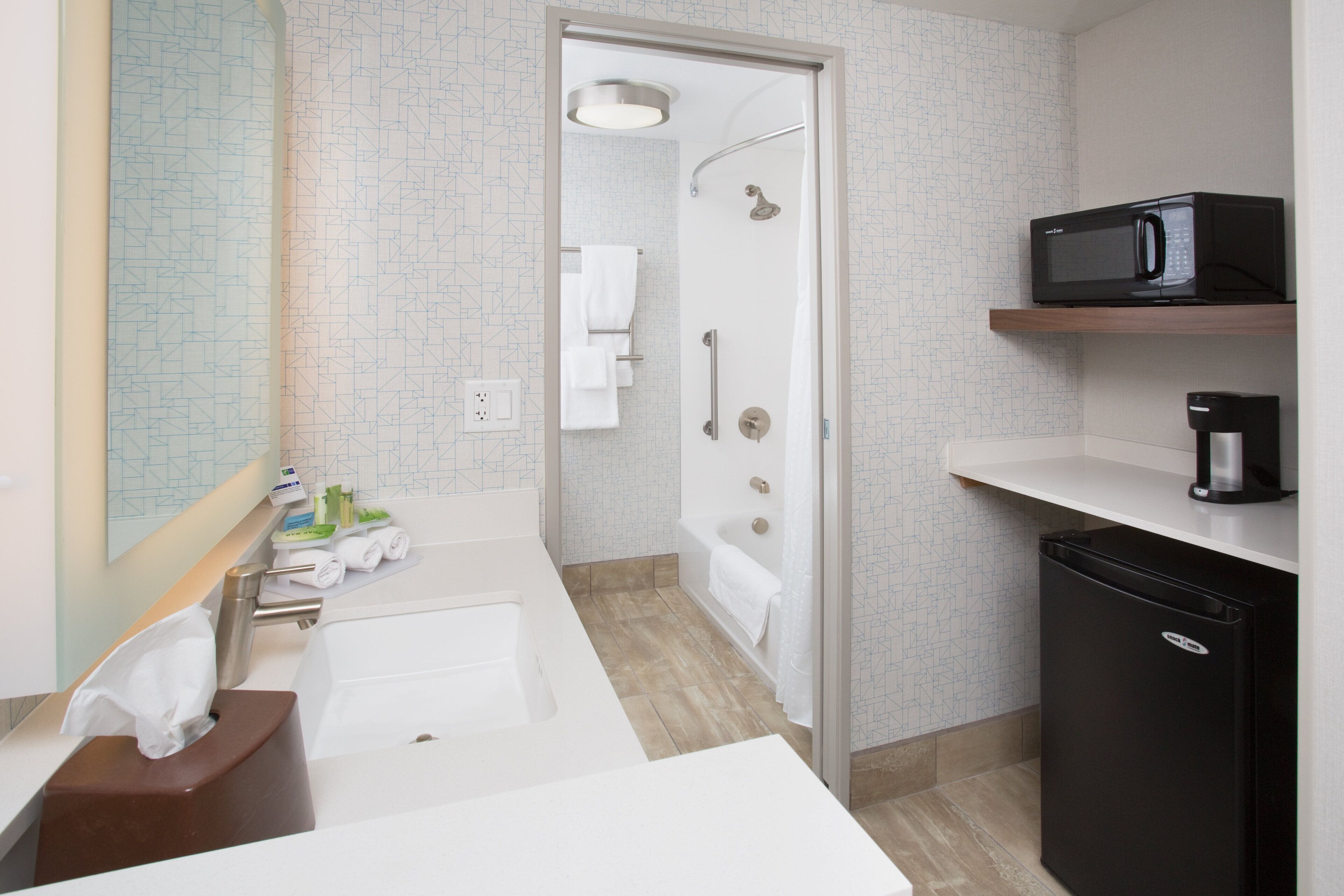 Ein modernes Badezimmer mit Dusche, Waschbecken, Toilette, einer Mikrowelle und einer Kaffeemaschine.
