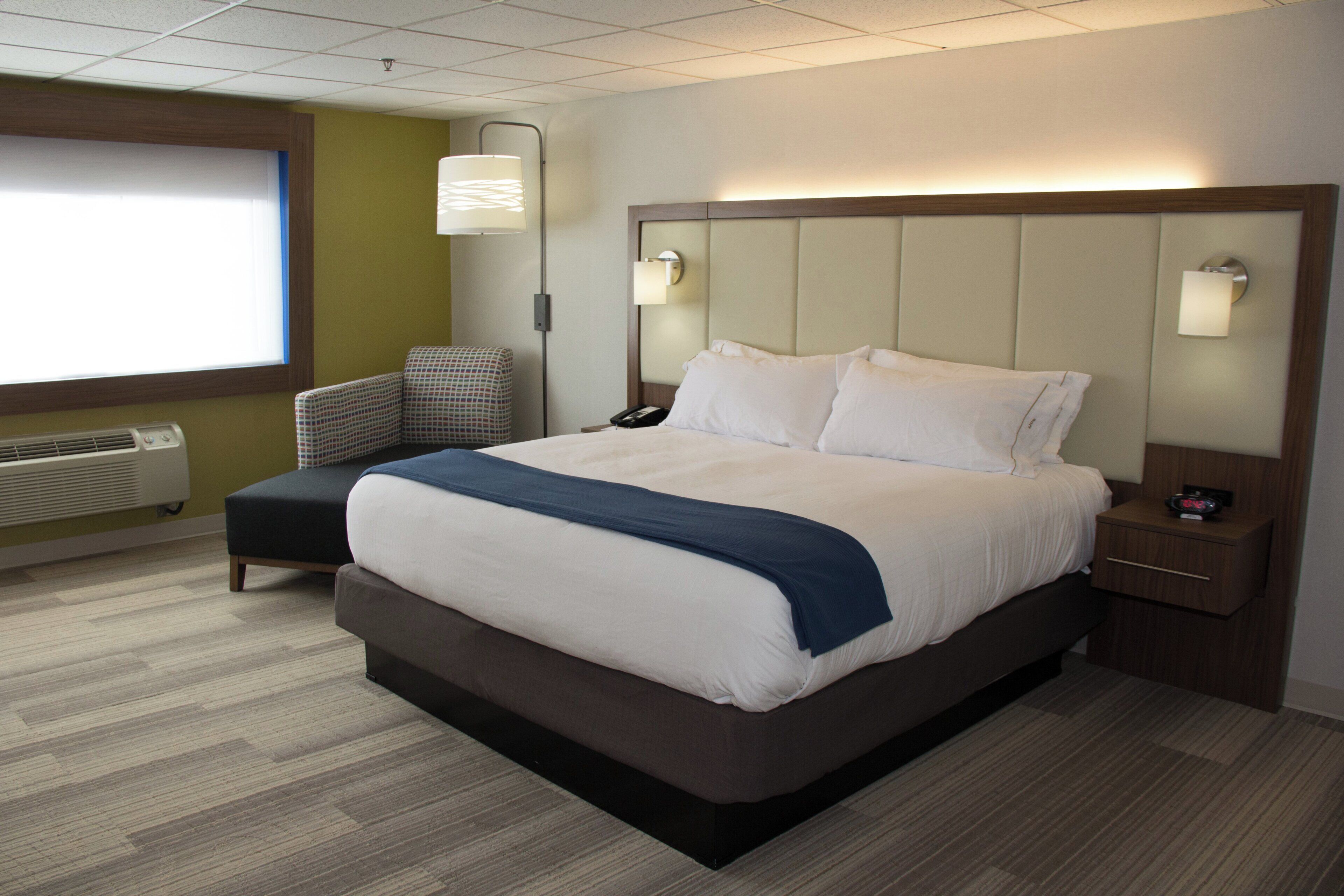 Une chambre d’hôtel avec un grand lit, une chaise, une table de chevet et une lampe.