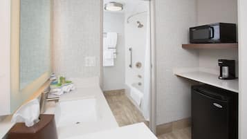 Un baño moderno con lavamanos, espejo, toallero, ducha y un microondas en un estante.