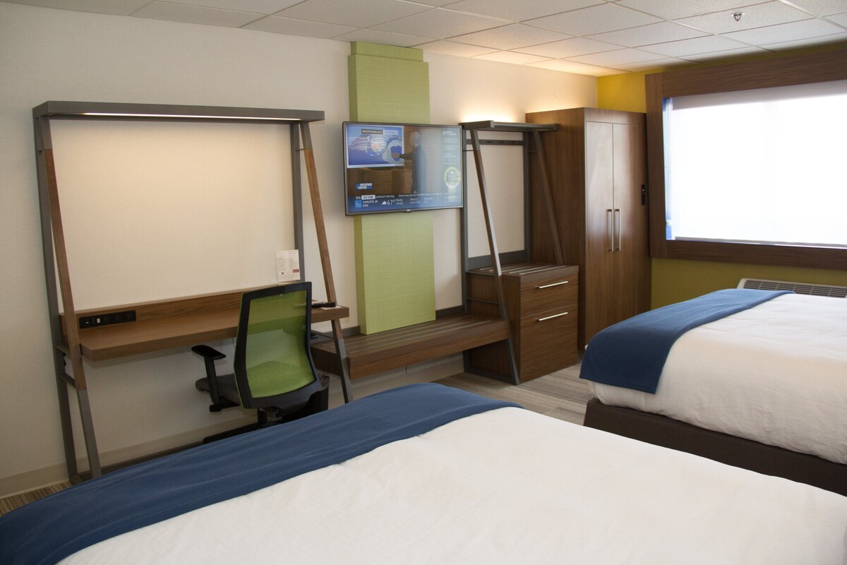 Une chambre d’hôtel avec deux lits, un bureau avec un ordinateur, un téléviseur fixé au mur et une armoire.