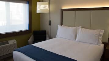 A hotel room with a large bed, a bedside table, a lamp, and a window with blinds.