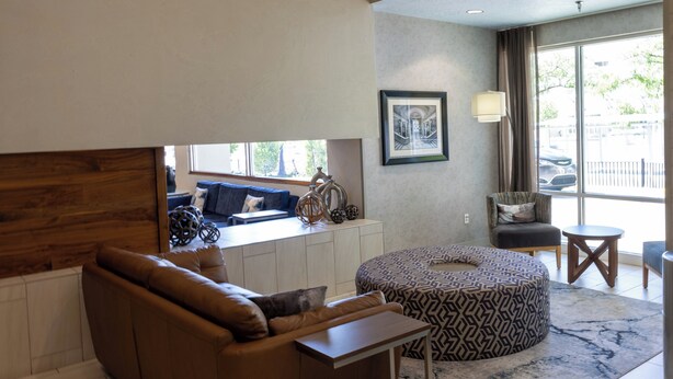 Una sala de estar moderna con un sofá de cuero marrón, un reposapiés estampado, una pared de acento de madera, una obra de arte enmarcada y vistas al exterior a través de grandes ventanales.