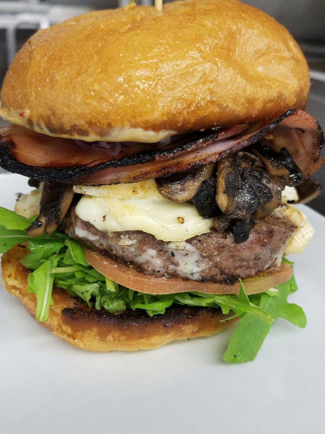 Um hambúrguer com pão tostado, bacon grelhado, cogumelos, queijo e alface.
