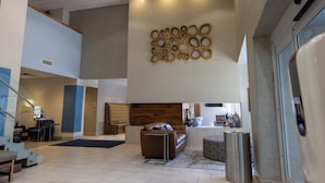 Un vestíbulo amplio con diseño moderno, que incluye una zona de estar con sofá y reposapiés, una escalera y una pared con elementos decorativos circulares.