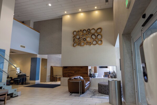 Um hall espaçoso com design moderno, apresentando uma área de estar com sofá e apoio para os pés, uma escada e uma parede com detalhes decorativos circulares.