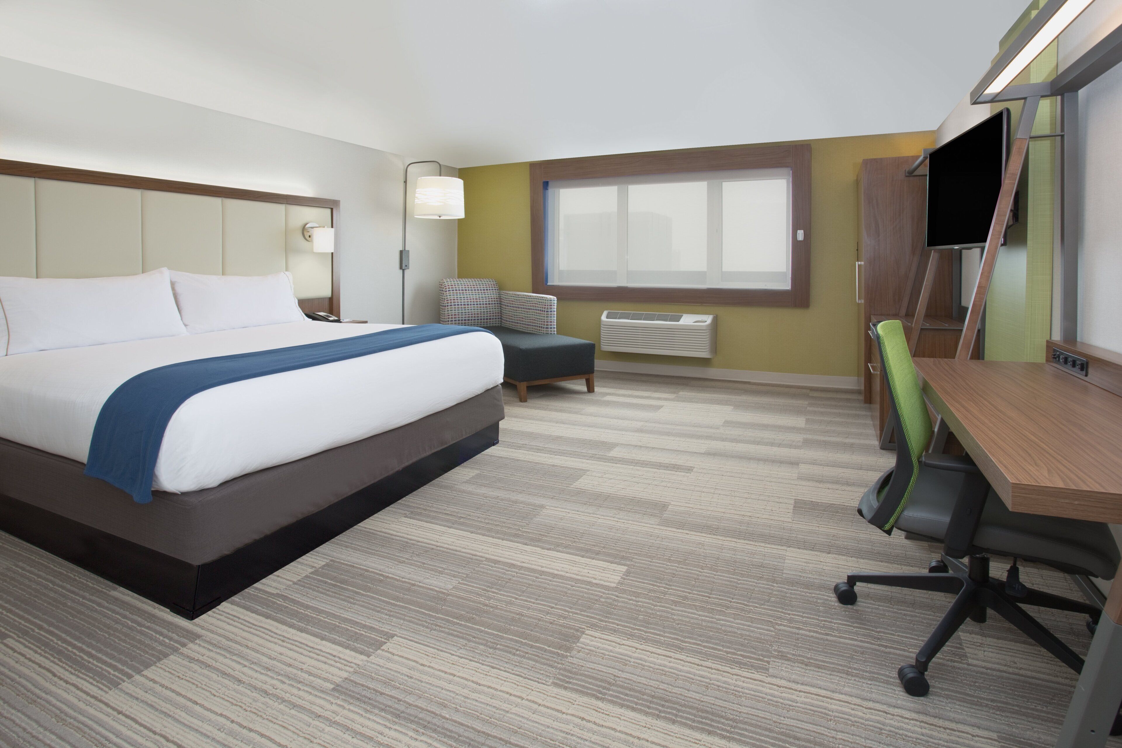 Habitación de hotel con cama, escritorio, silla, lámpara y ventana.
