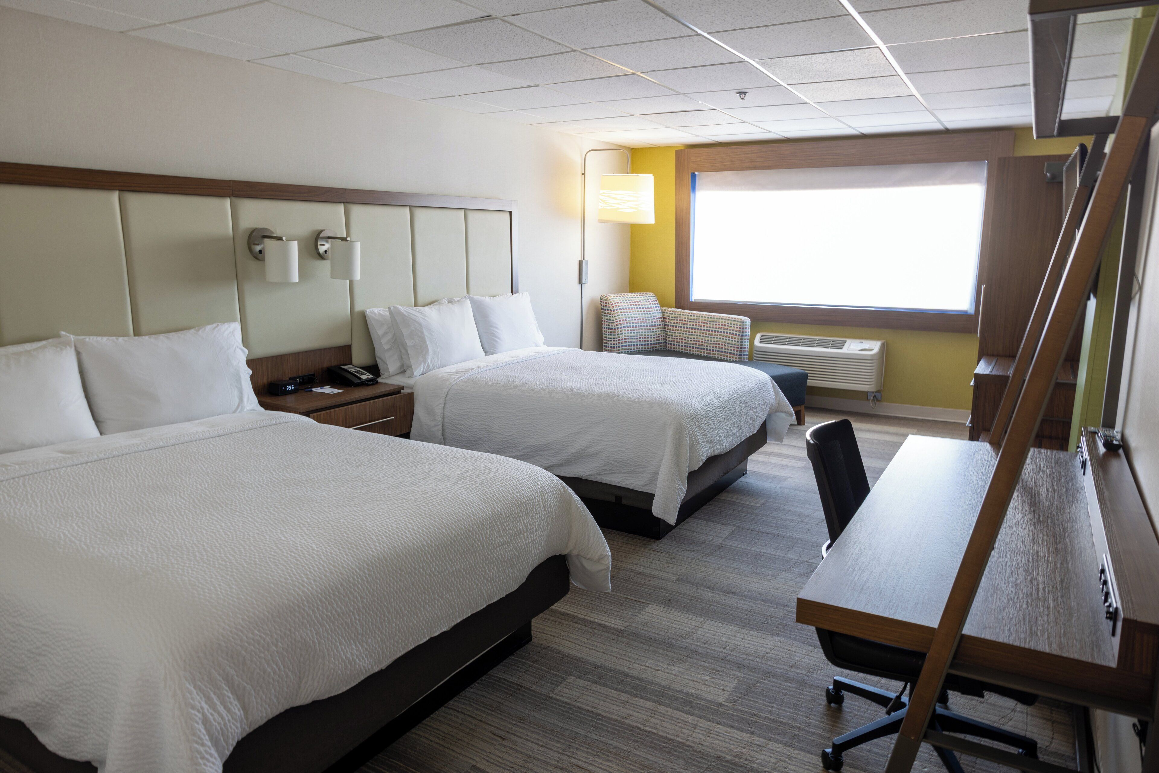A hotel room with two beds, a desk, and a window with natural light.