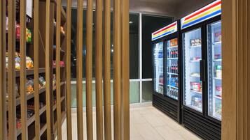 A grocery store interior with wooden shelving stocked with snacks and a refrigerated display case with beverages.