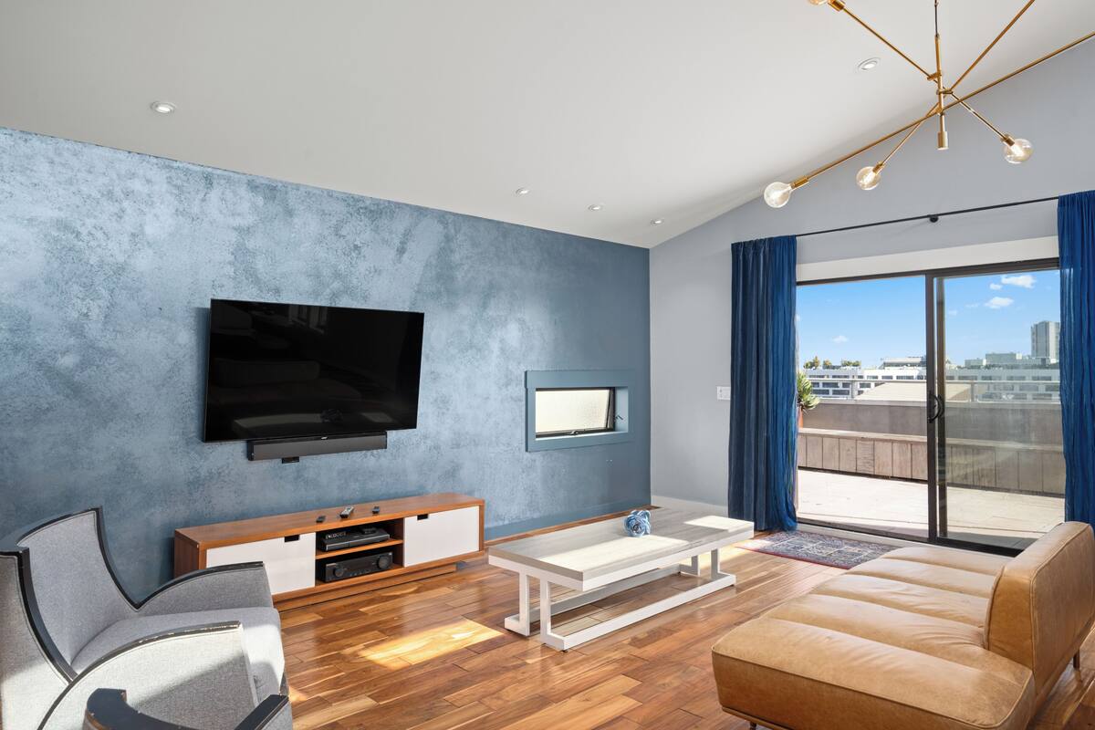 A modern living room with a flat-screen TV, a sofa, a coffee table, and a sliding glass door leading to a balcony.