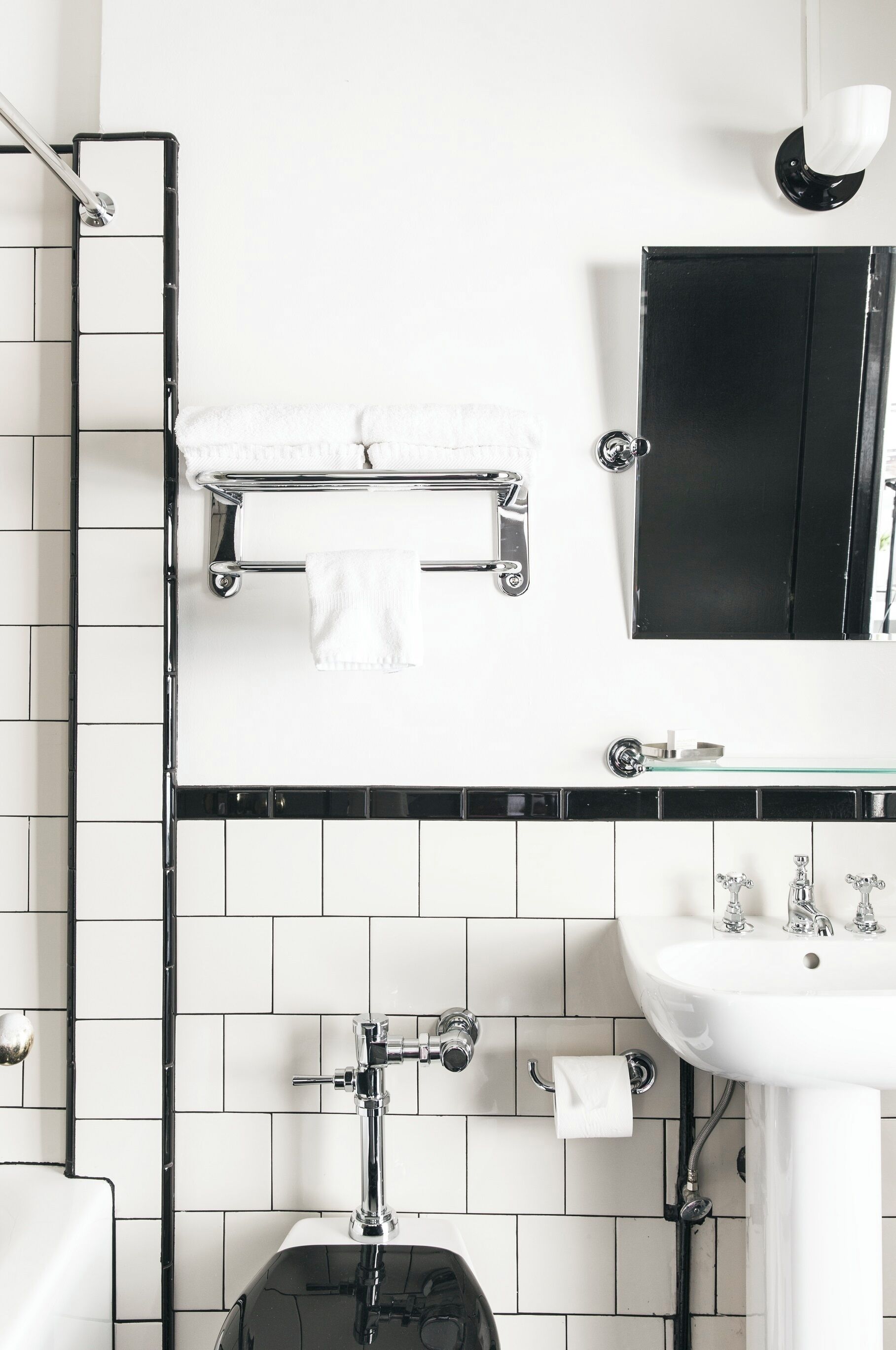 A modern bathroom with a white and black tiled backsplash, a white sink with chrome fixtures, and a black cabinet above the mirror.
