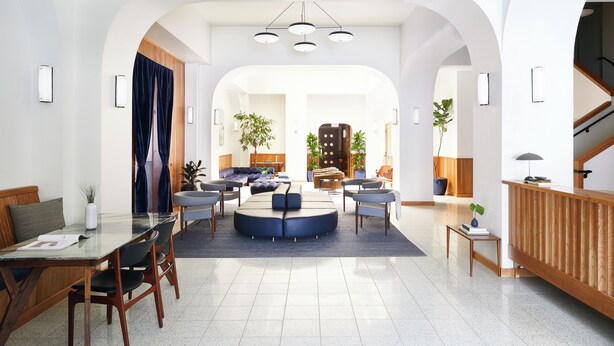 A spacious living area with a round seating arrangement, a wooden reception desk, and a staircase. - Tilden Hotel (San Francisco)