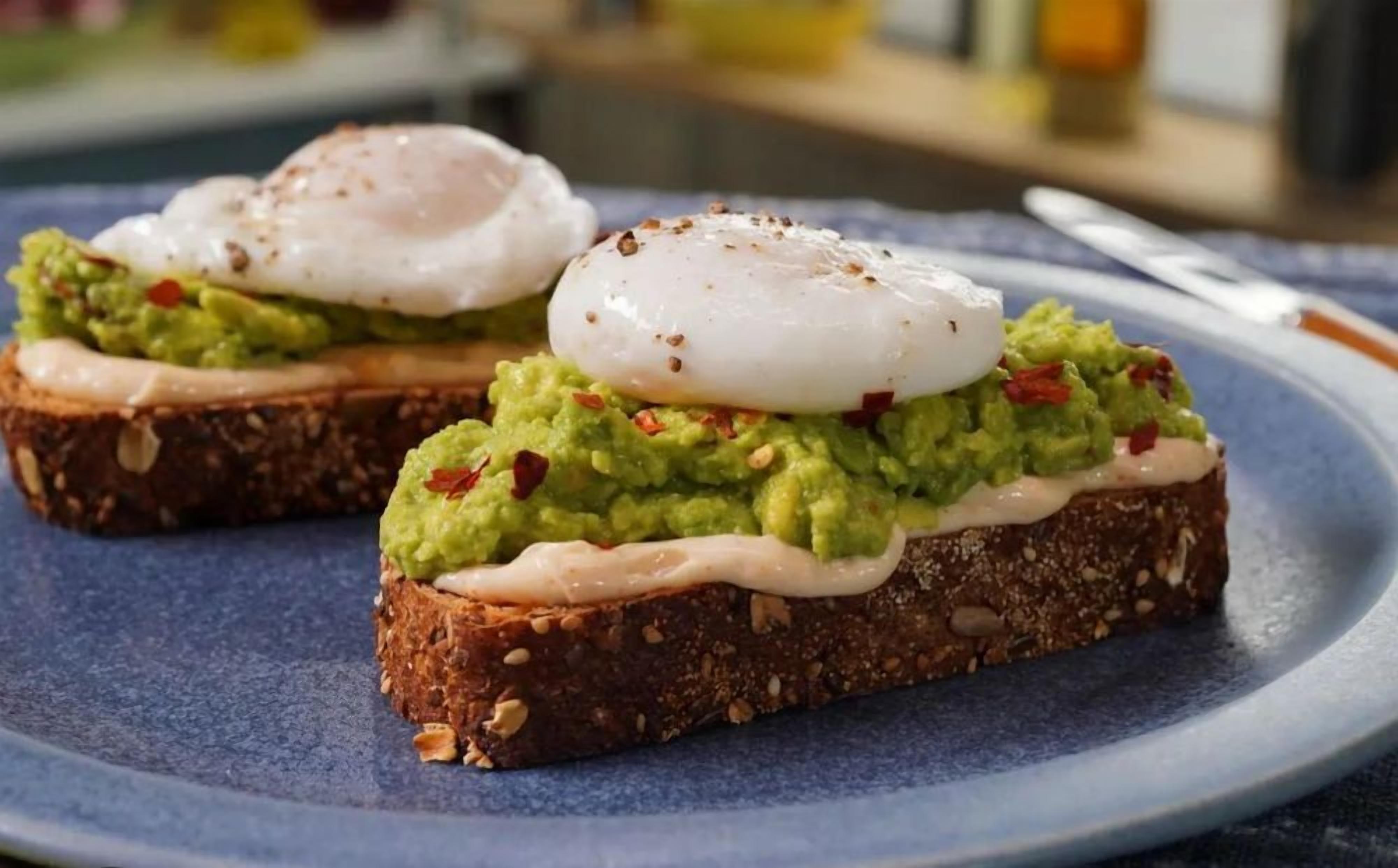 Two pieces of toast topped with avocado, a poached egg, and red pepper flakes on a blue plate.