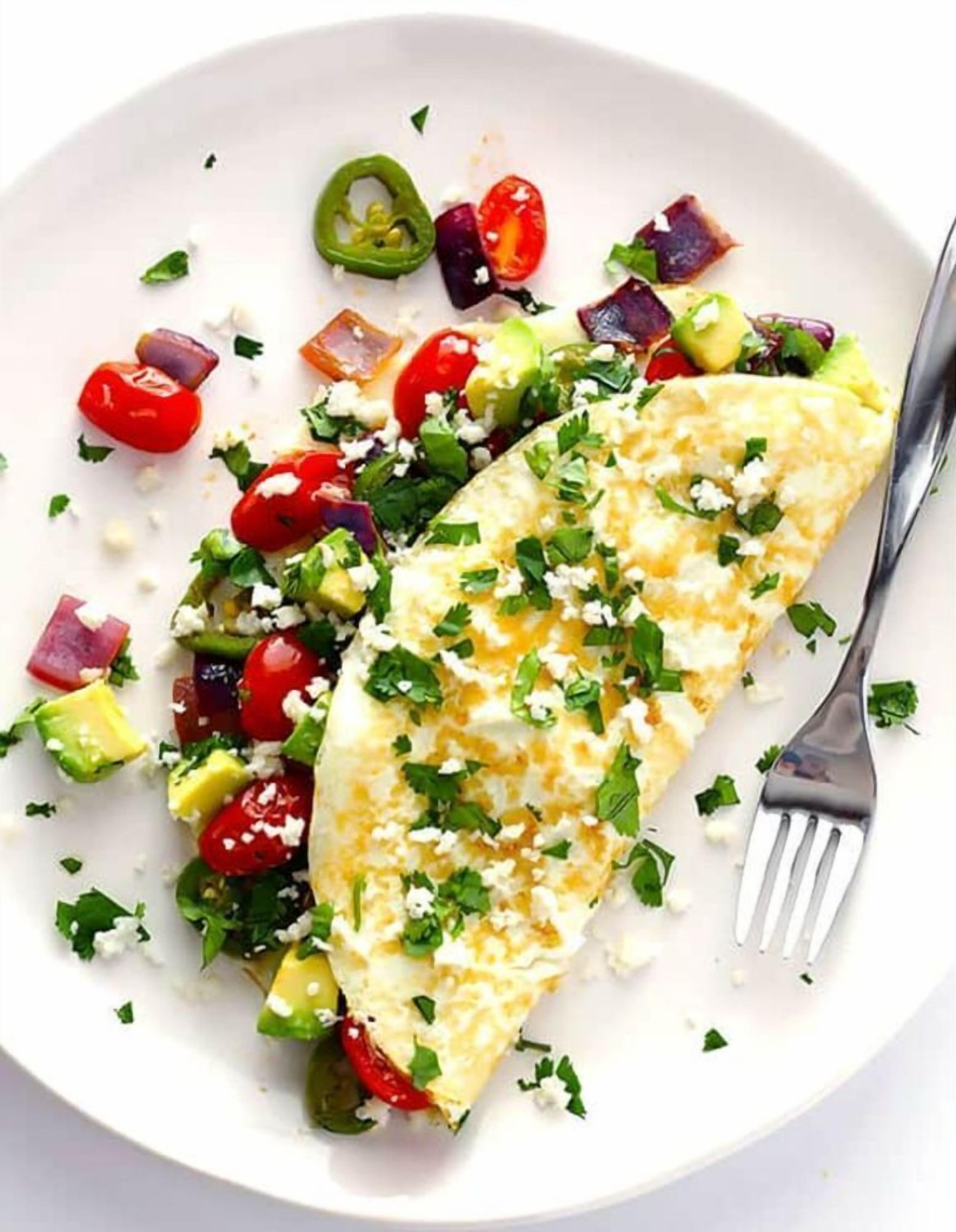 A plate with an omelette, tomatoes, avocado, and feta cheese.