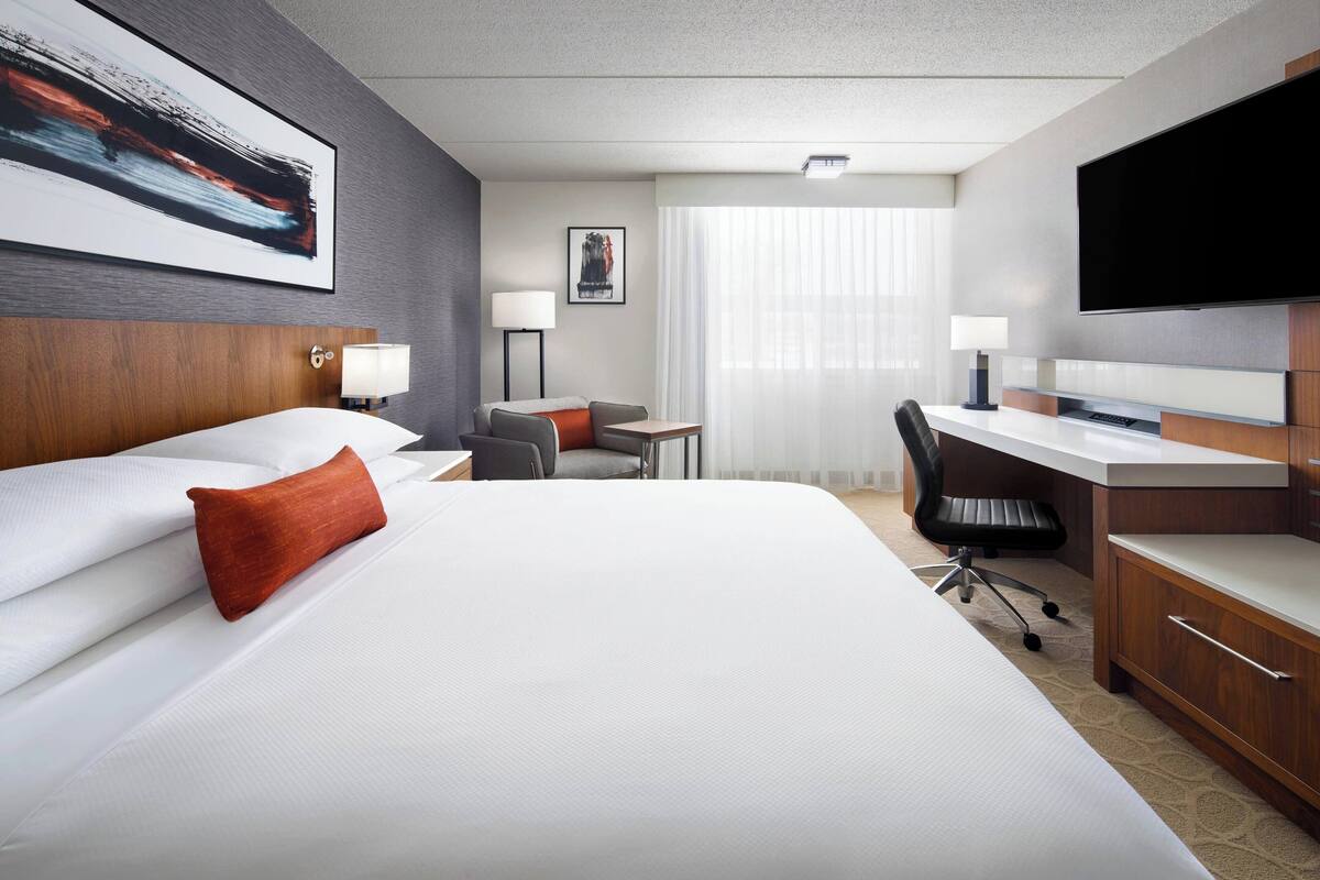 A hotel room with a large bed, a desk, a chair, a TV, and a window with curtains.