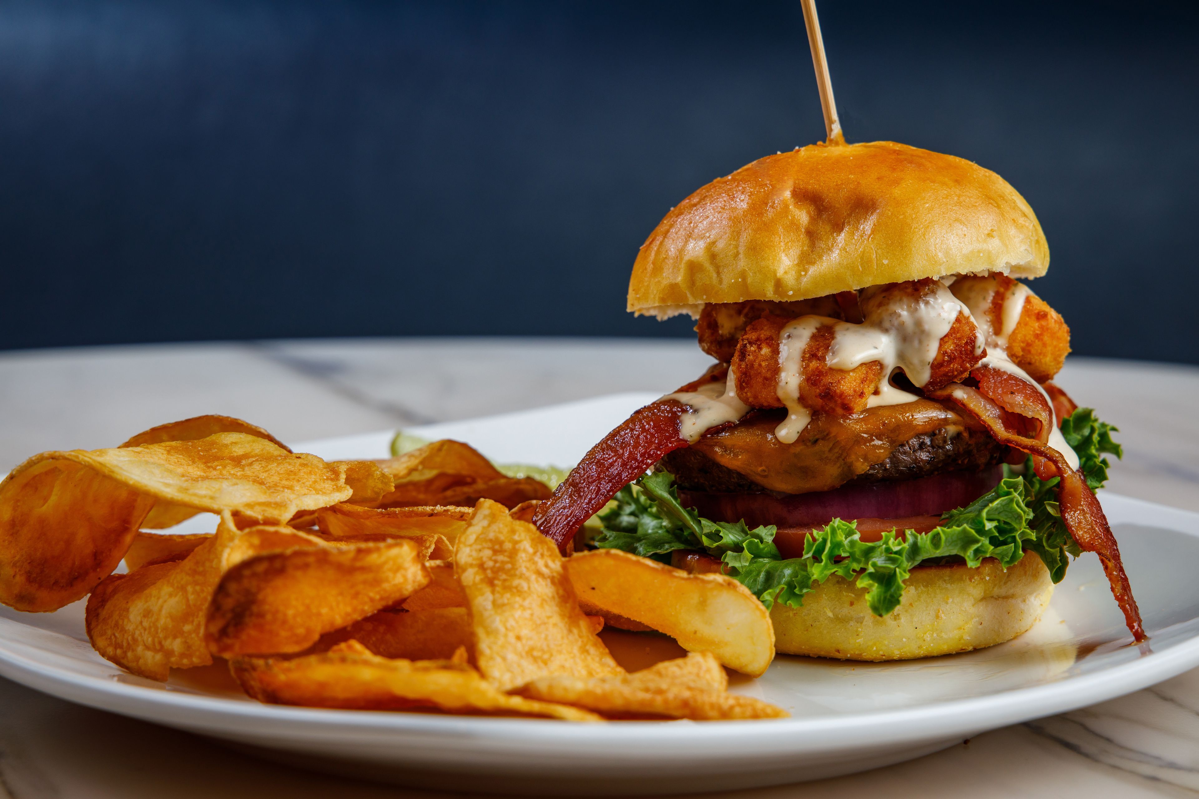 Un hamburger garni de bacon, de laitue et servi dans un pain, accompagné de chips sur une assiette.