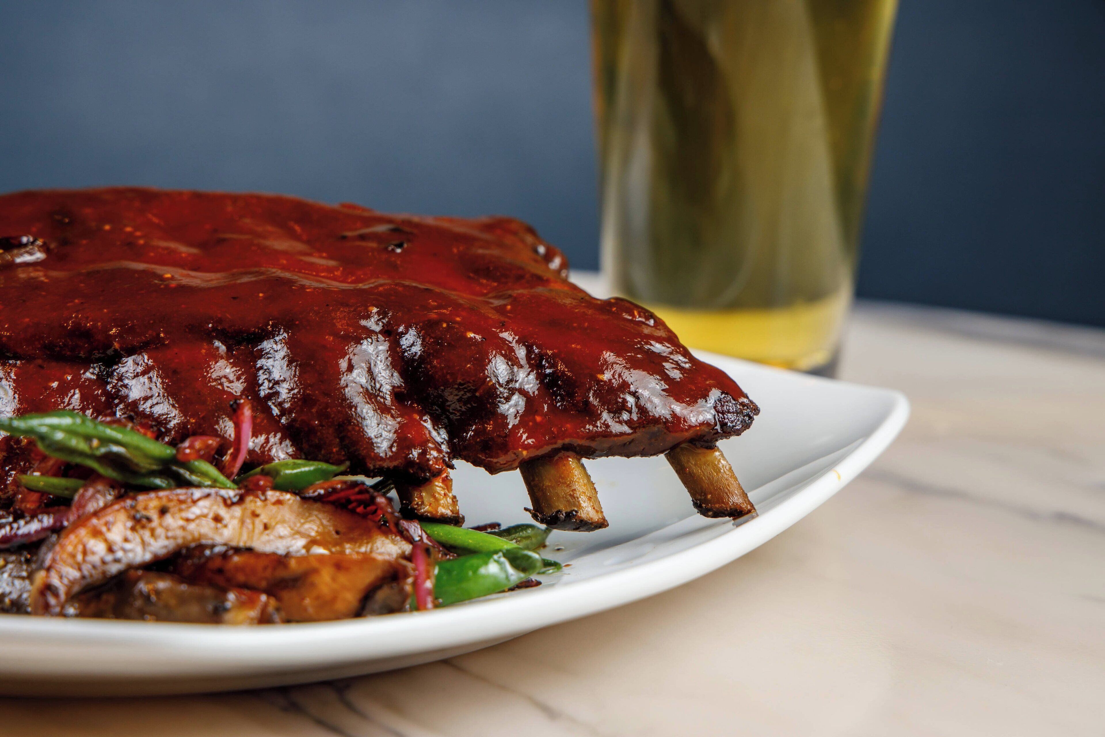 Un plato de costillas a la parrilla con verduras y una cerveza.