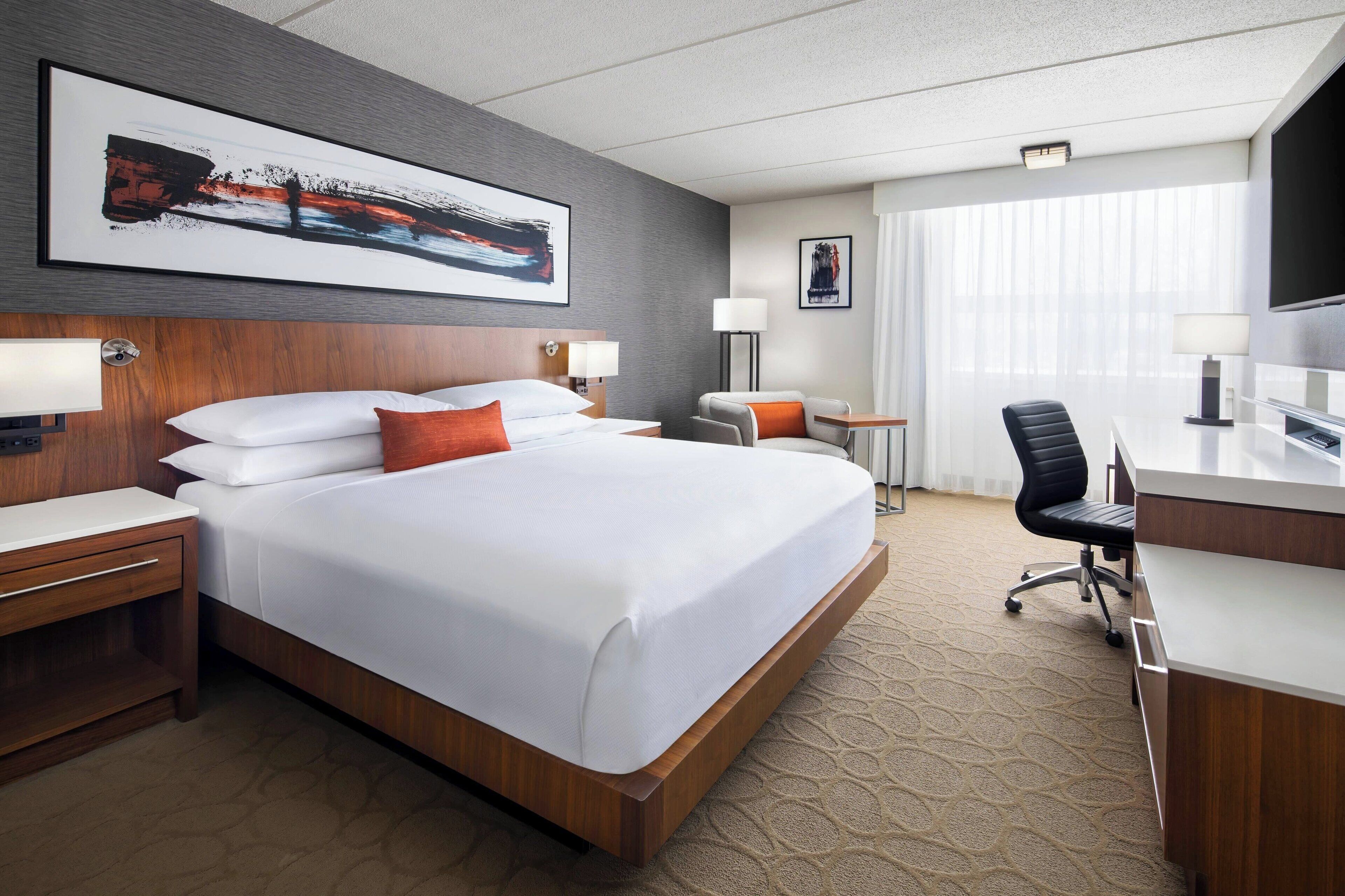 A hotel room with a large bed, a desk, a chair, and a TV.