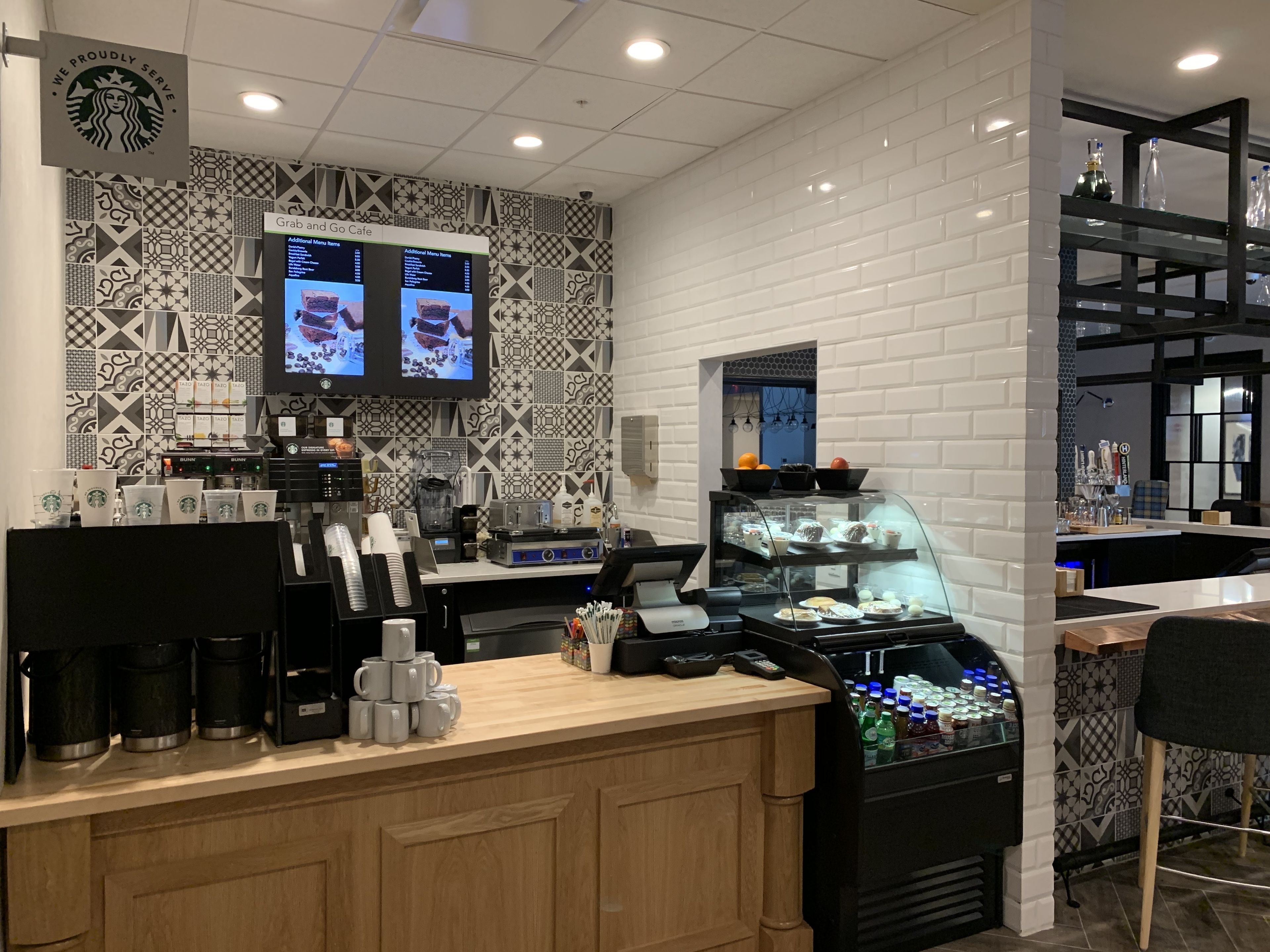 A Starbucks coffee shop interior with a modern design, including a counter with a coffee machine, a display of pastries, and a menu screen.