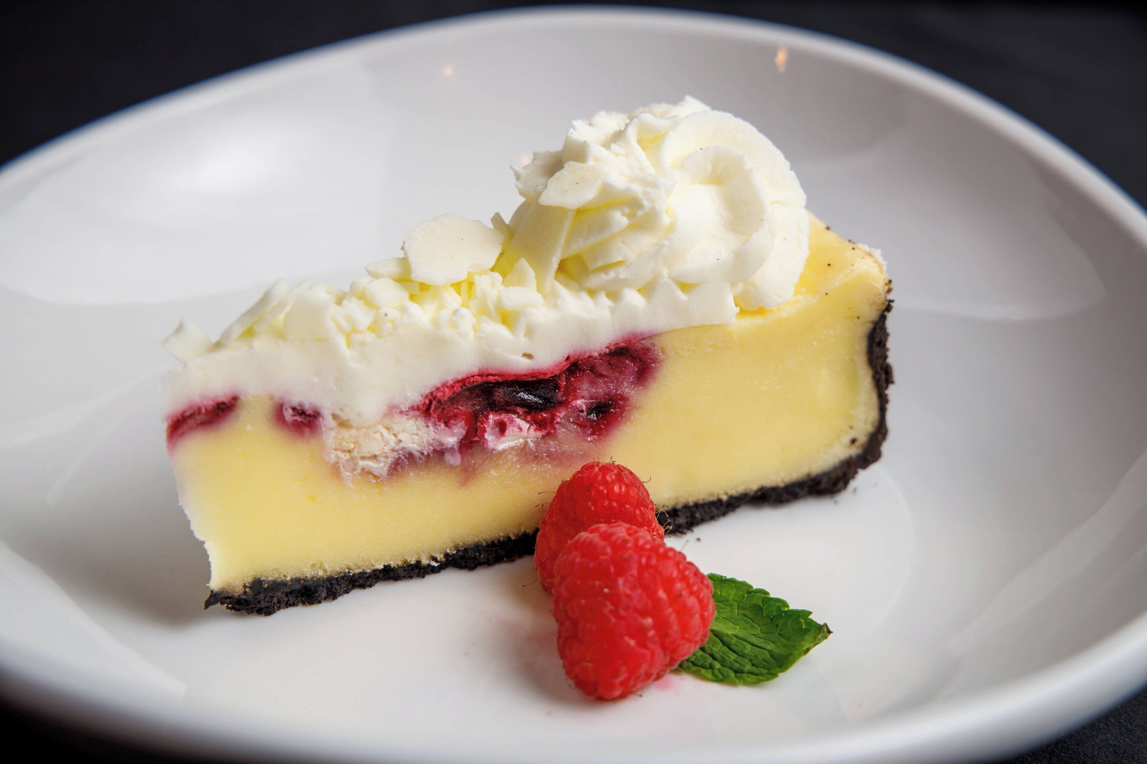 A slice of cheesecake with whipped cream and raspberries on a white plate.