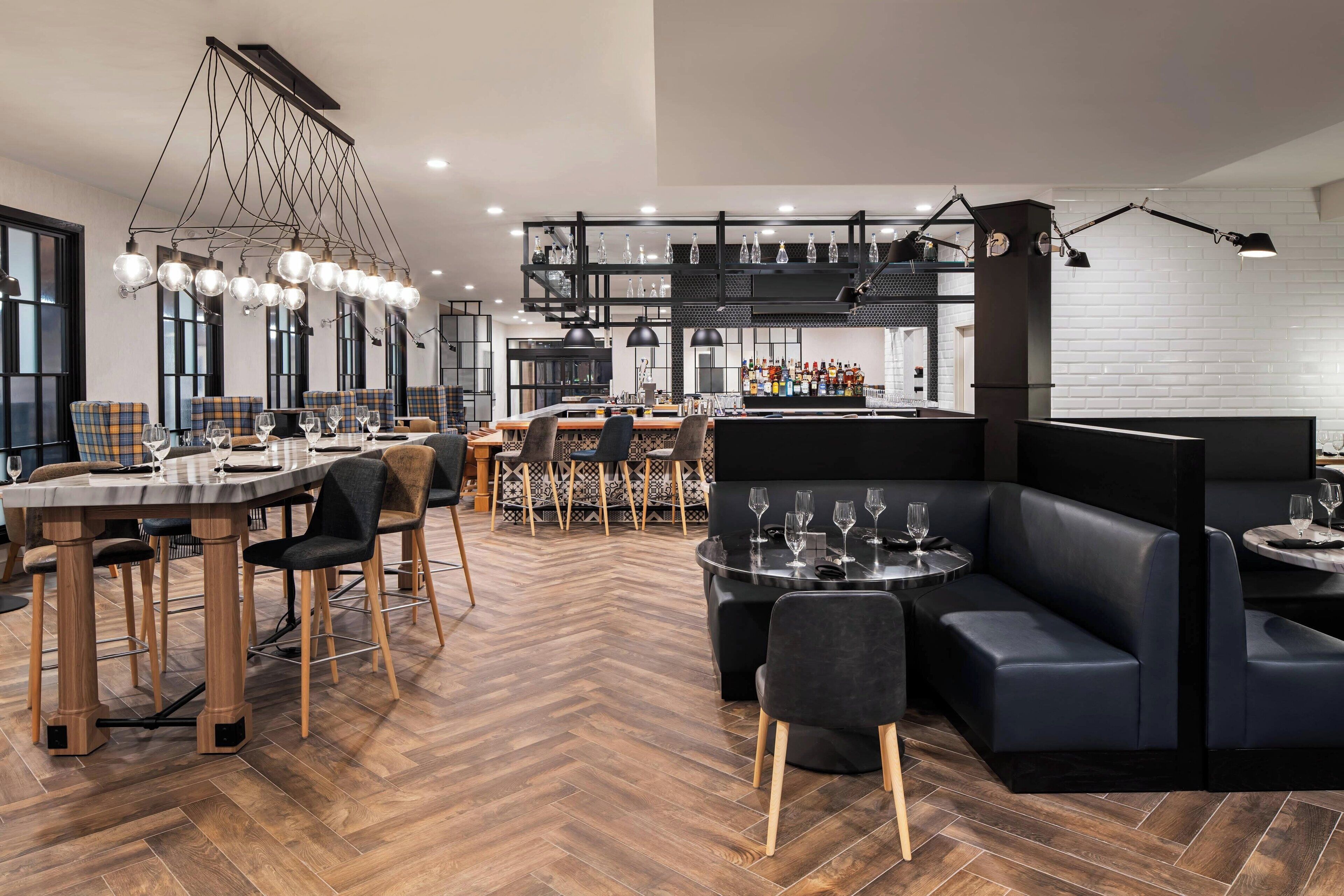 Un restaurante moderno con suelo de espiga, mesas de madera y asientos tapizados en negro.