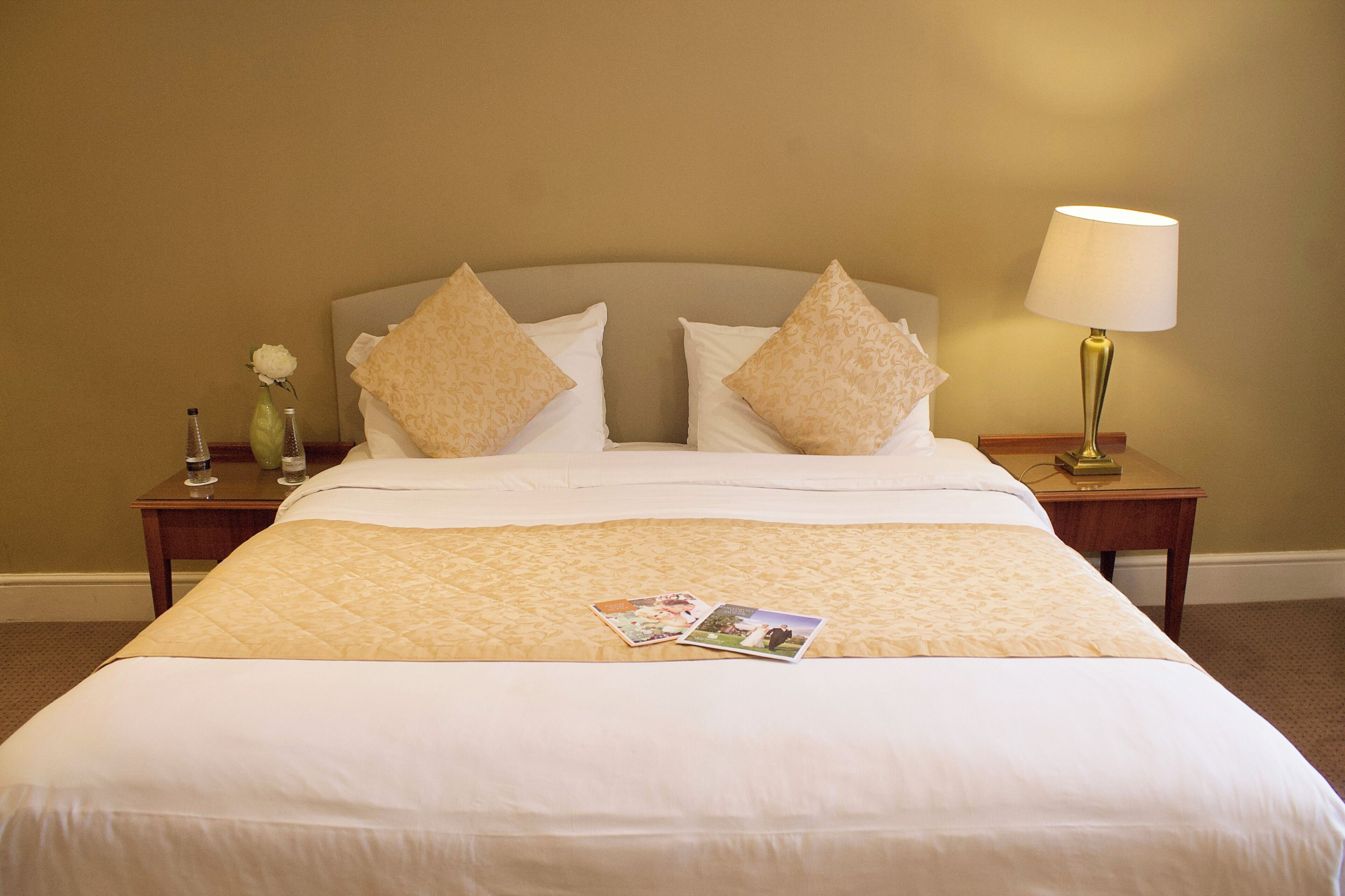 A neatly made bed with a quilted bedspread, two pillows, and a bedside table with a lamp.