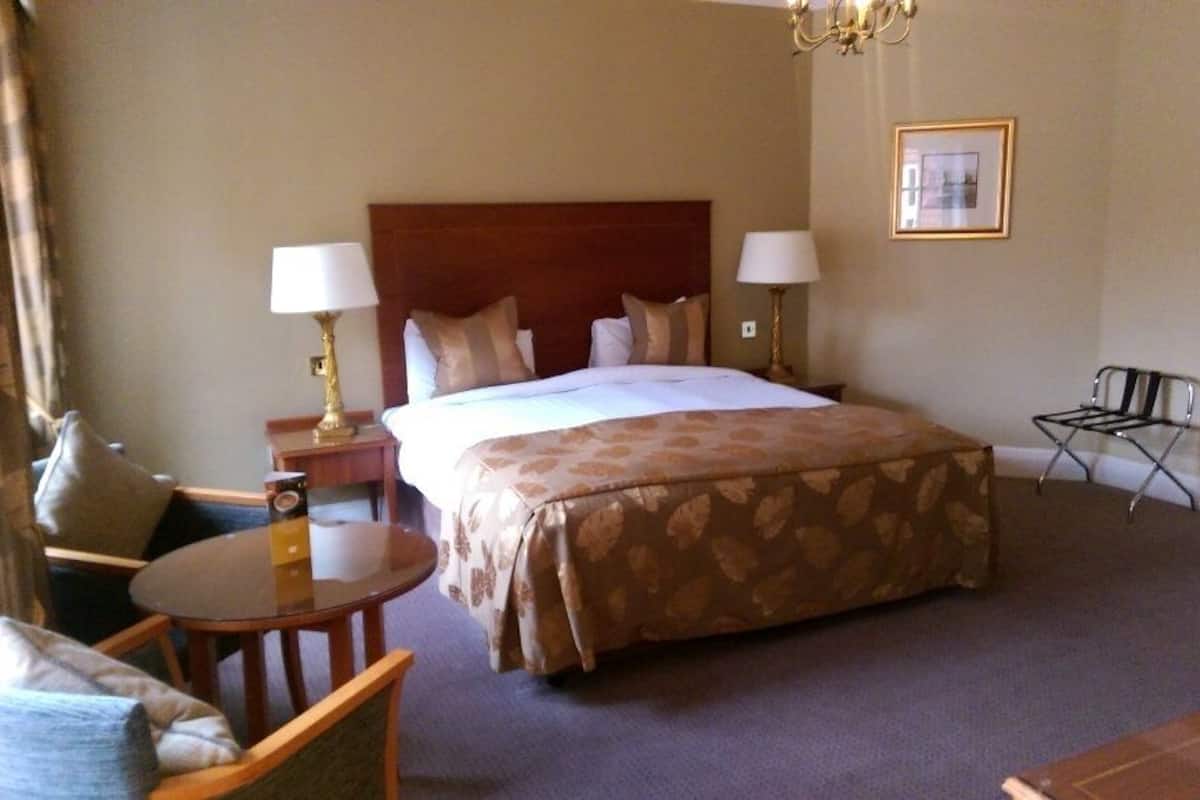 A hotel room with a large bed, two bedside lamps, a small round table, a chair, a desk, and a television.