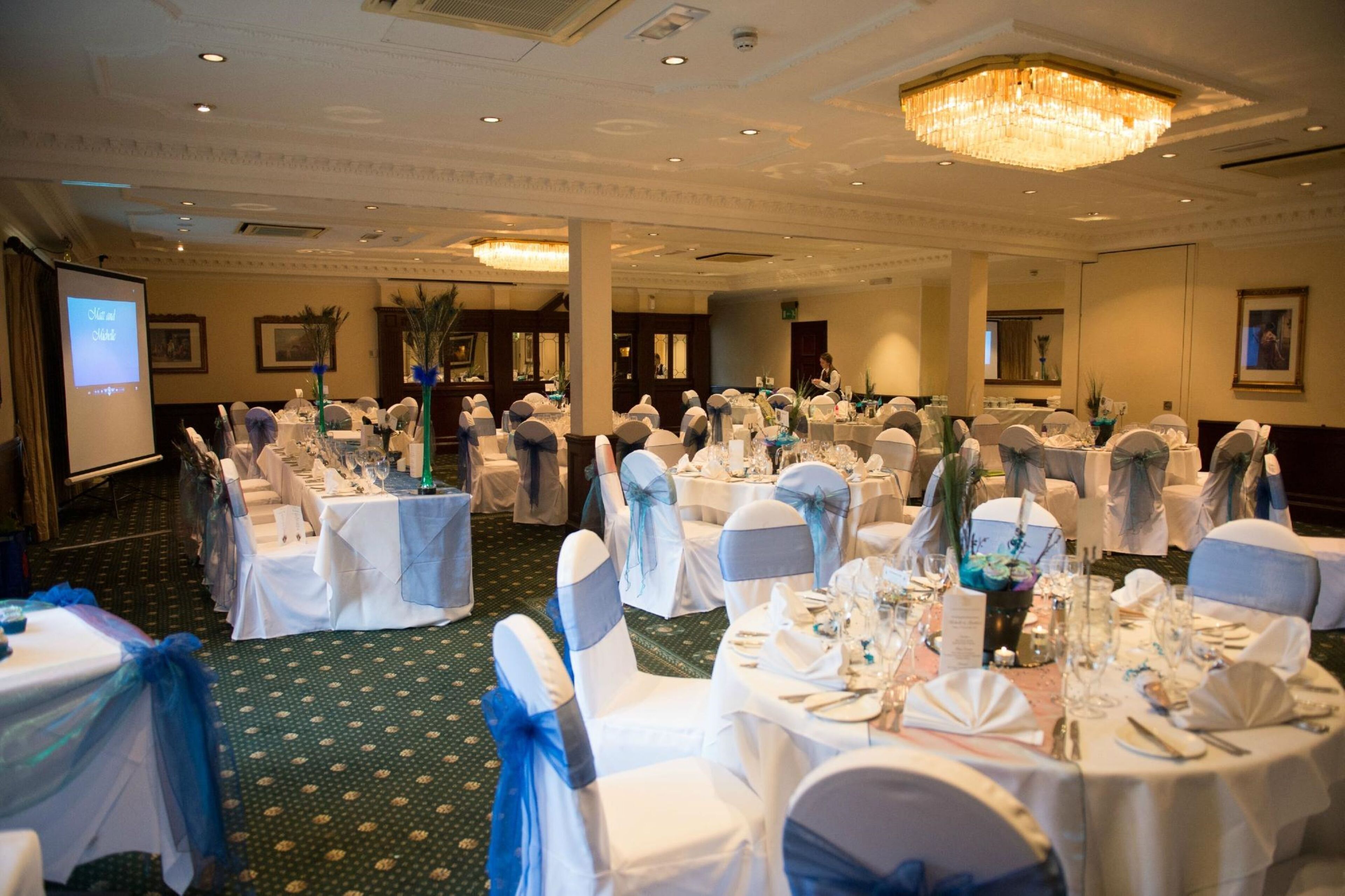 Un salón de banquetes con mesas redondas, manteles blancos y cintas azules.