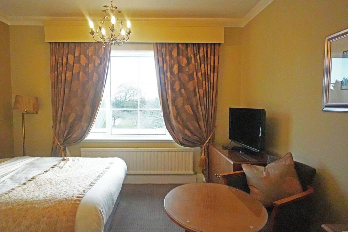A hotel room with a bed, a television, a chair, a table, and a window with curtains.