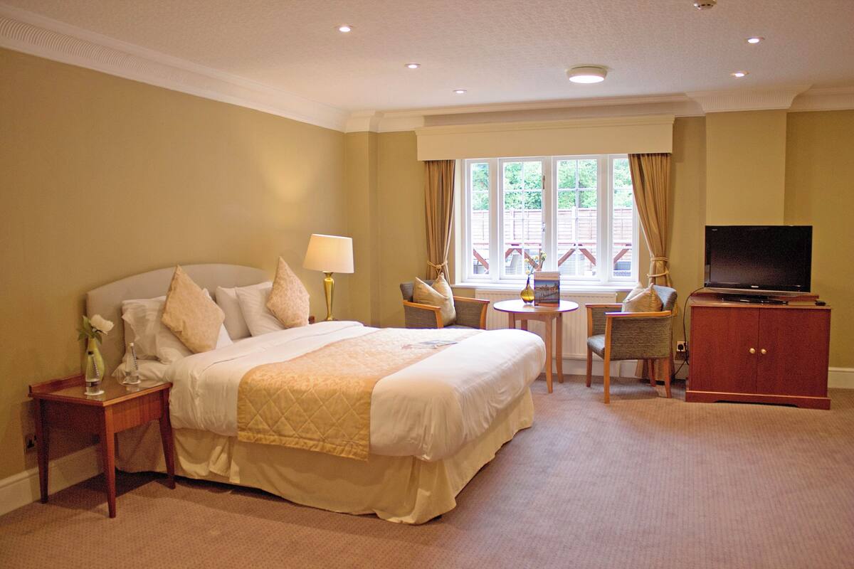 A hotel room with a bed, a TV, a small table, and a window with curtains.
