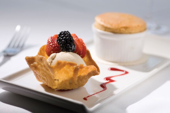 A dessert with berries and a scoop of ice cream on a plate, accompanied by a small pastry and a container of cream.