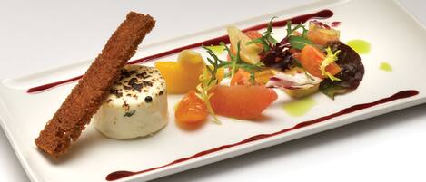 A white rectangular plate with a dessert consisting of a breaded item, a dollop of cream, and a colorful salad with various vegetables and a drizzle of sauce.