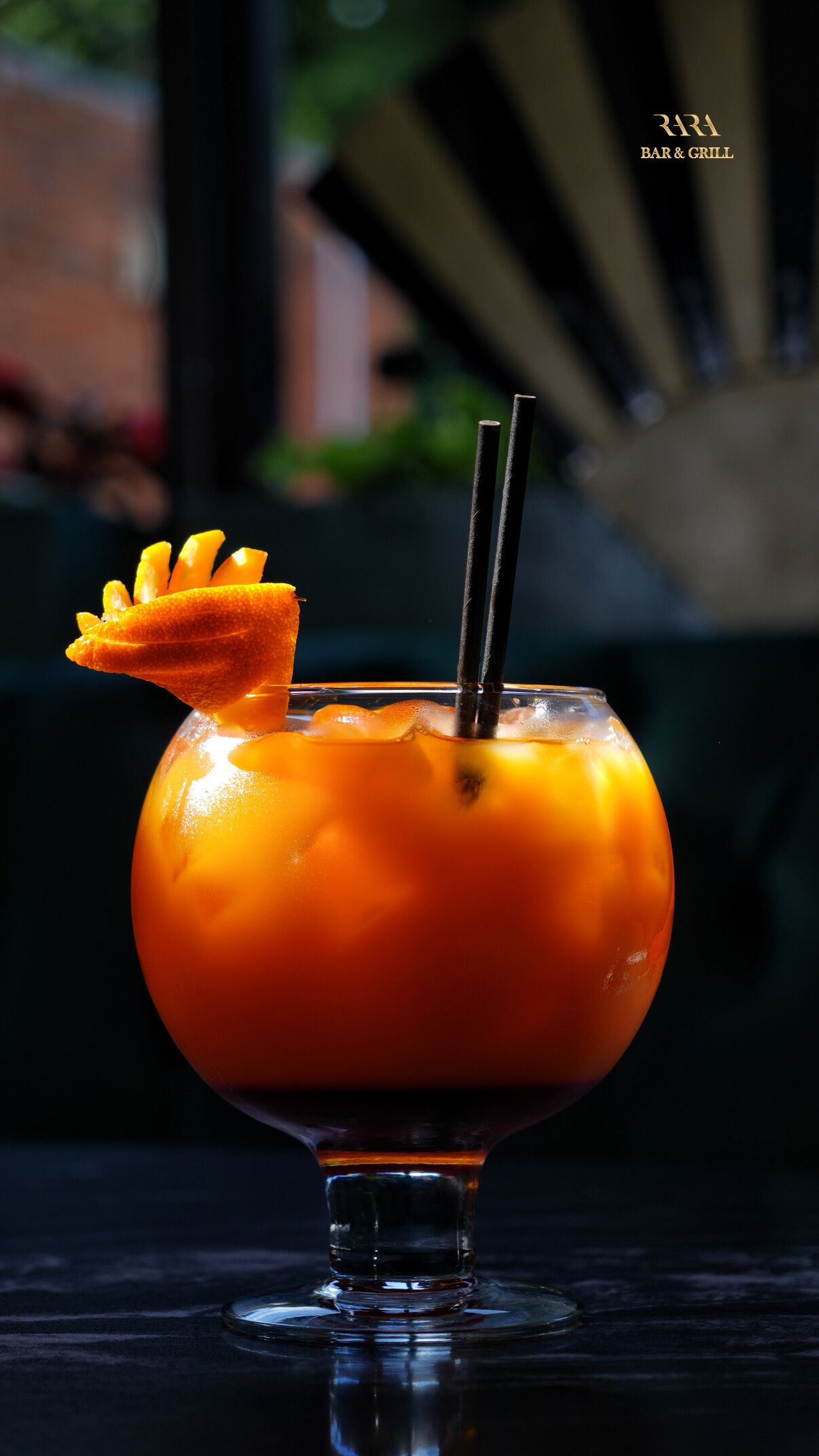 A cocktail in a stemmed glass with a garnish, a straw, and a dark background.