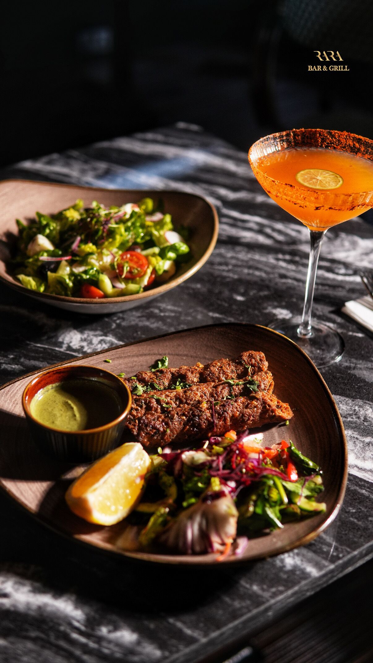 A meal with grilled meat, salad, and a margarita on a dark table.