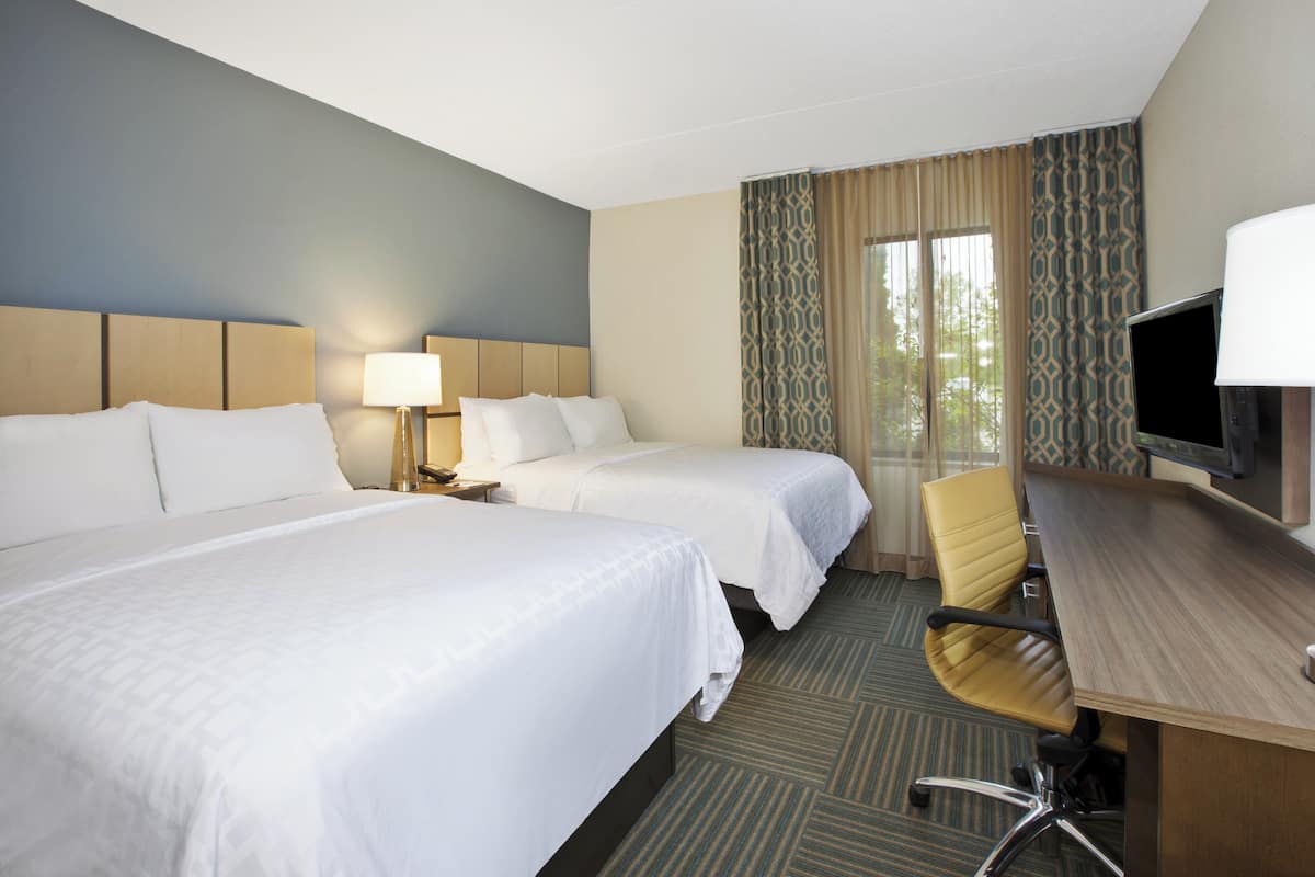 A hotel room with two beds, a desk with a chair, a TV, and a window with curtains.