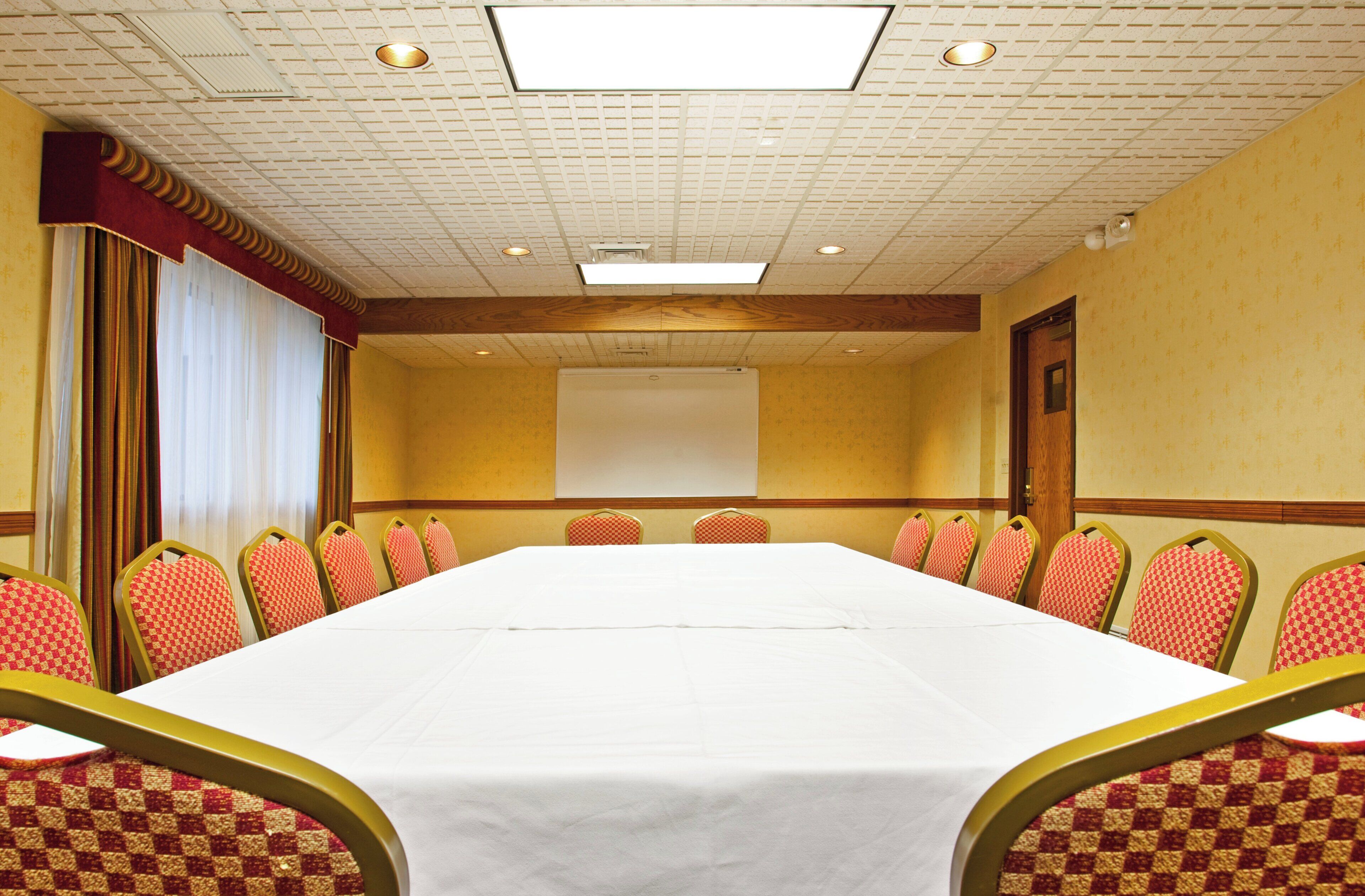 Une salle de conférence avec une longue table, des rangées de chaises, un écran de projection et un mur décoré de motifs.