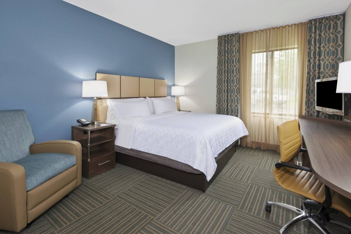 A hotel room with a bed, a desk, a chair, a sofa, and a TV.