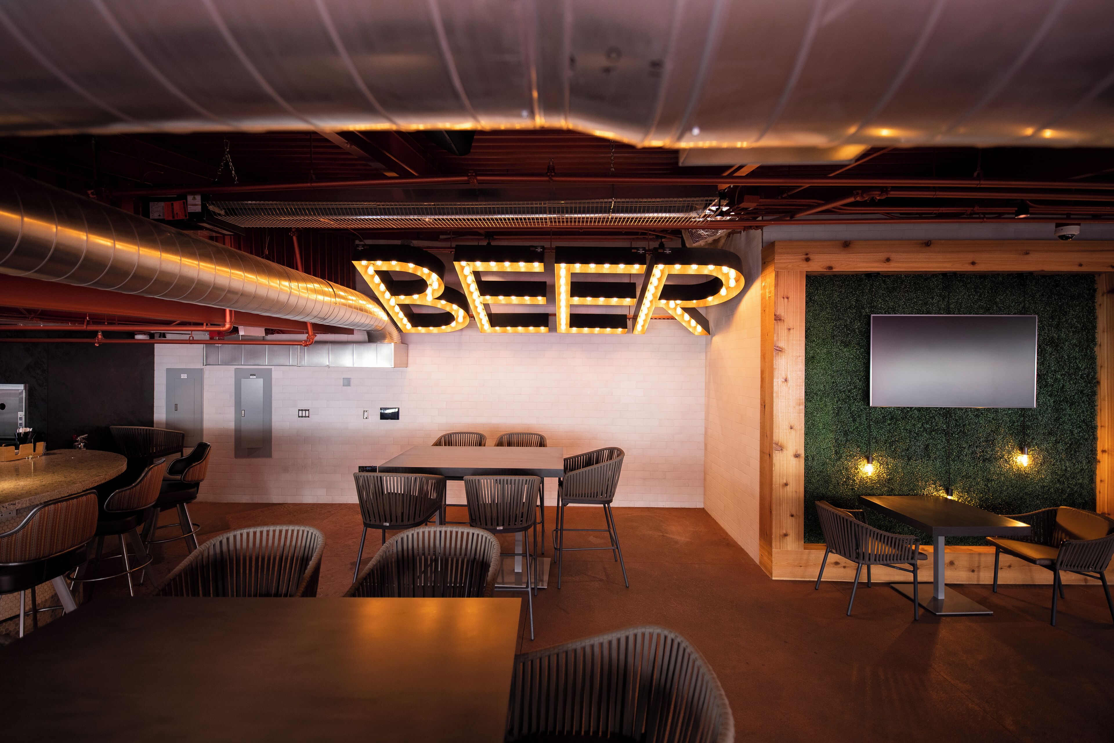 A modern bar area with a 'BEER' sign, a large table, and several chairs.