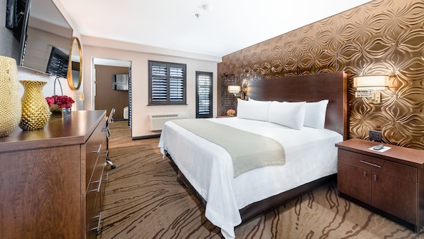 A hotel room with a large bed, a wooden dresser, a television, and a patterned wall. - Ellis Island Hotel (Las Vegas)