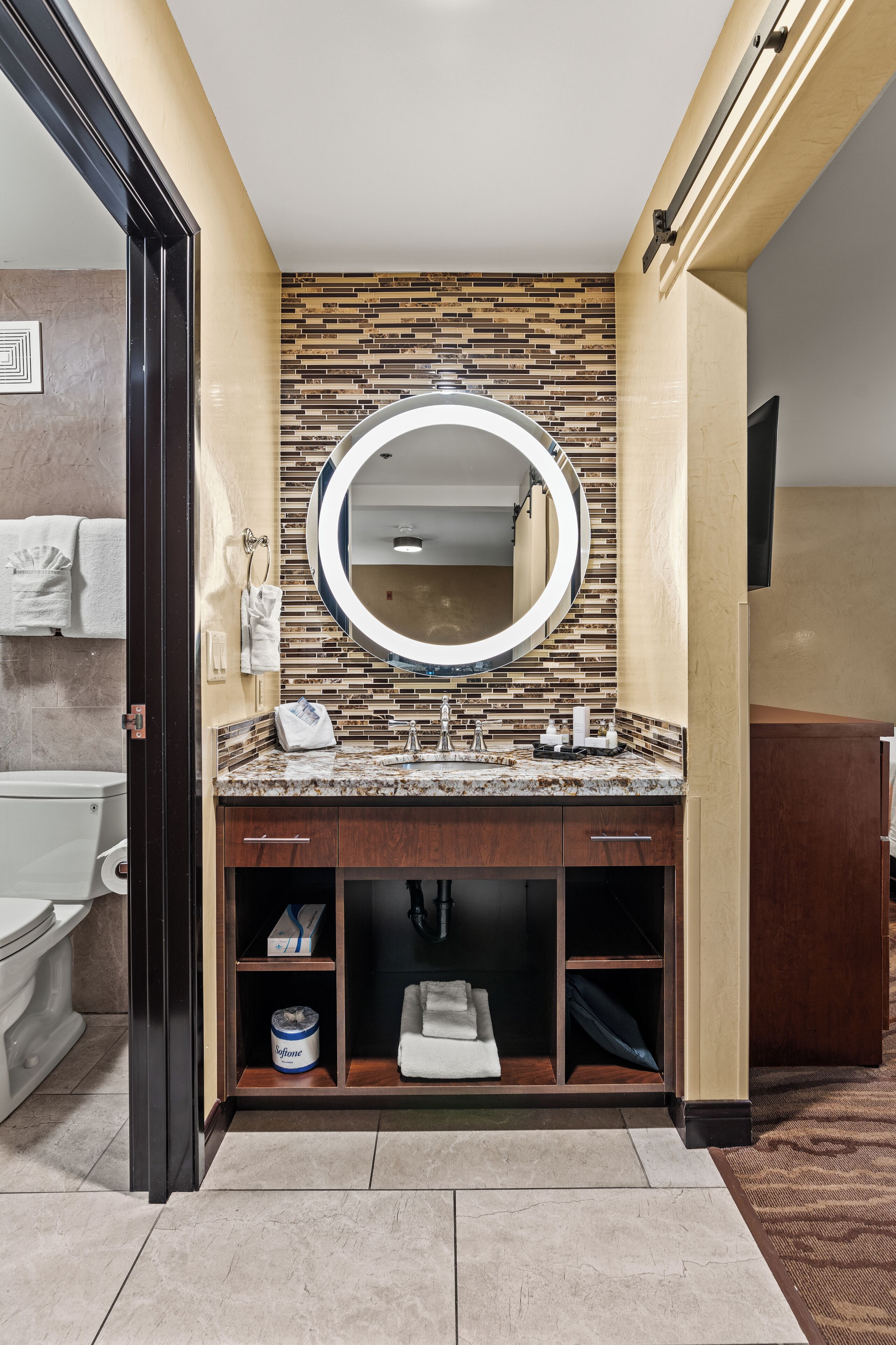 A modern bathroom with a granite countertop, a large mirror, and a tiled backsplash.