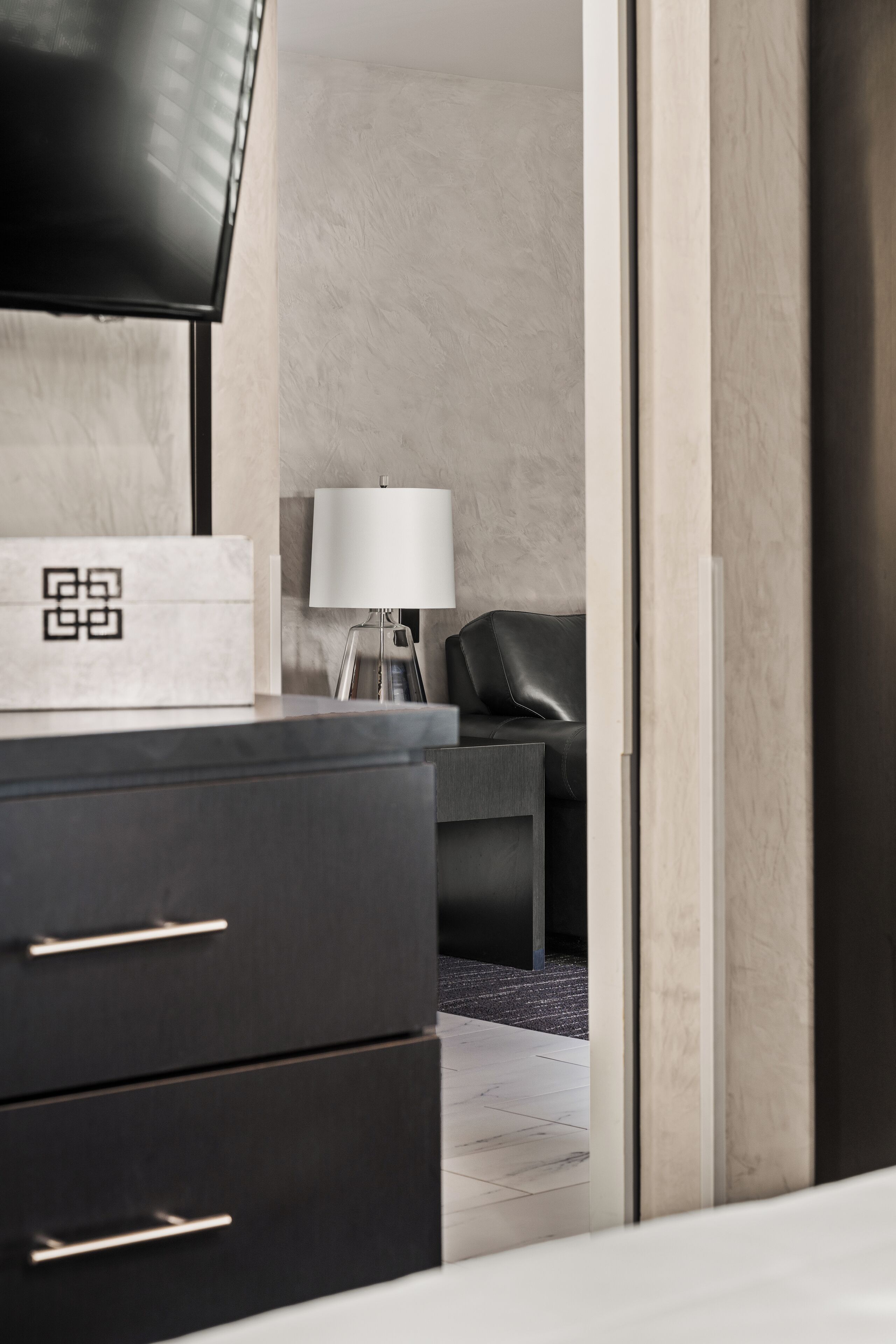 Une chambre d’hôtel moderne avec une commode en bois foncé, un téléviseur à écran plat et une lampe.