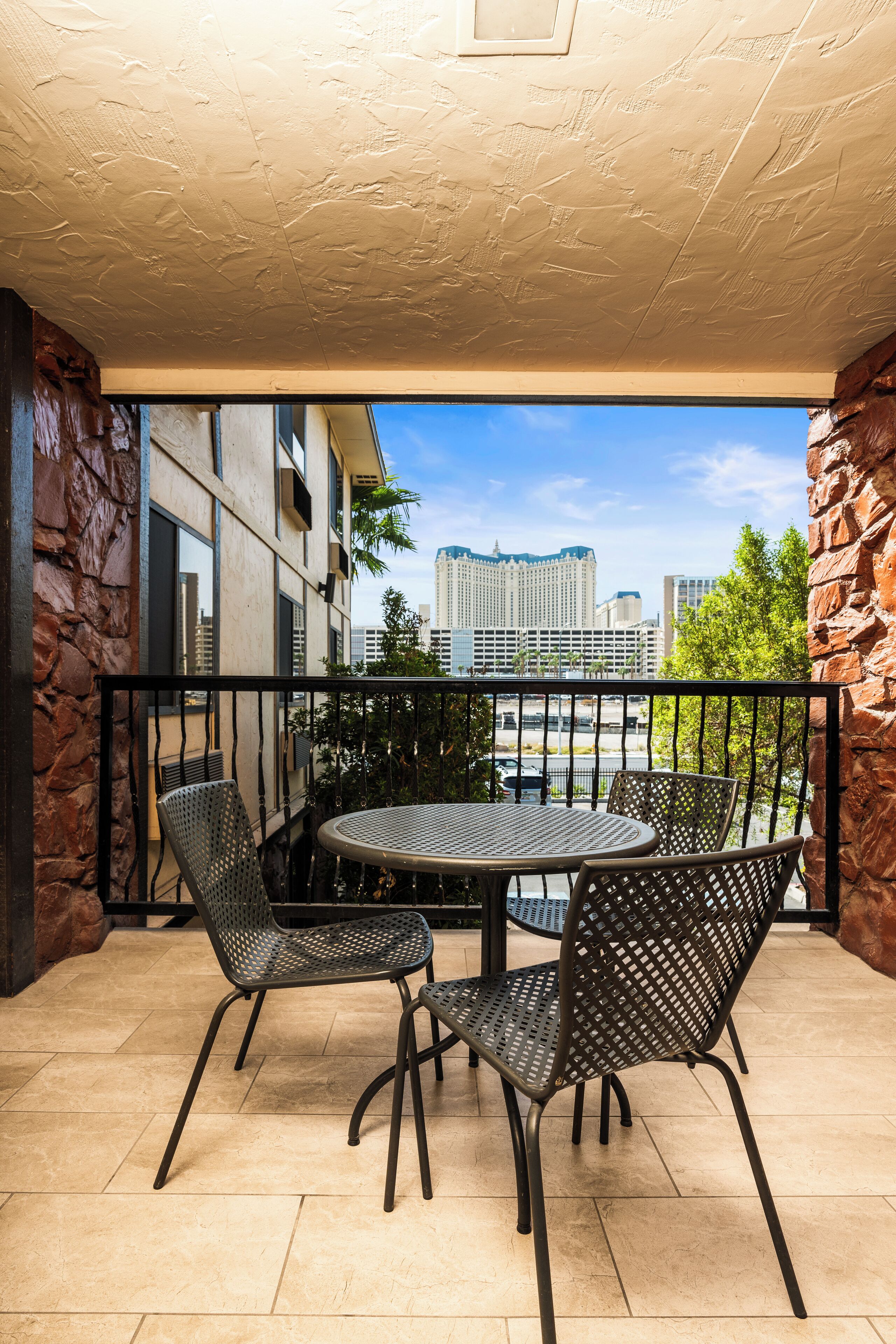 Un balcon avec une table ronde et deux chaises, donnant sur un paysage urbain avec des bâtiments et un ciel dégagé.