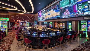 A bar area with multiple screens displaying sports events, a bar counter, and several red bar stools. - Ellis Island Hotel (Las Vegas)