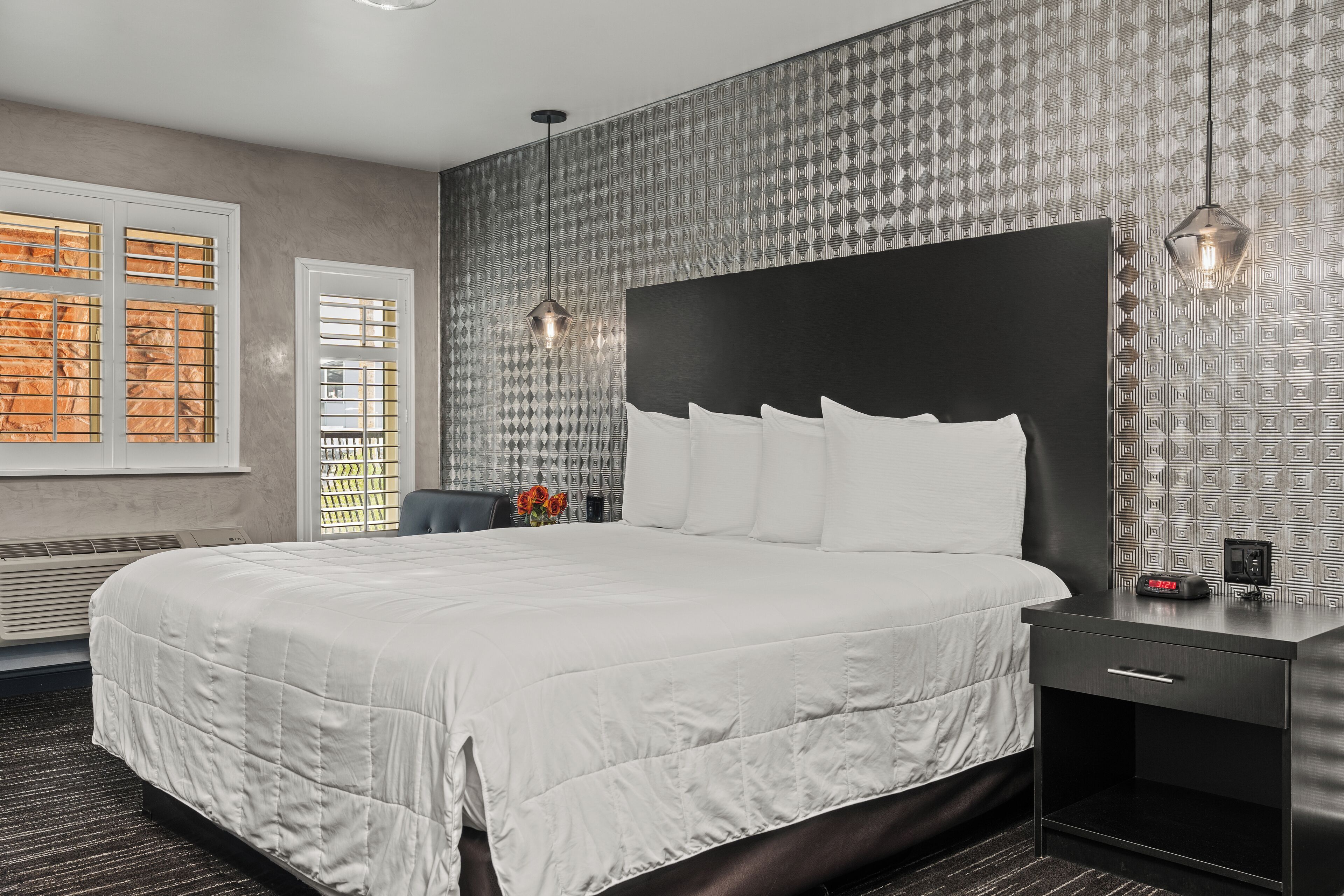 A modern hotel room with a large bed, a bedside table with a clock, and a patterned wallpaper.