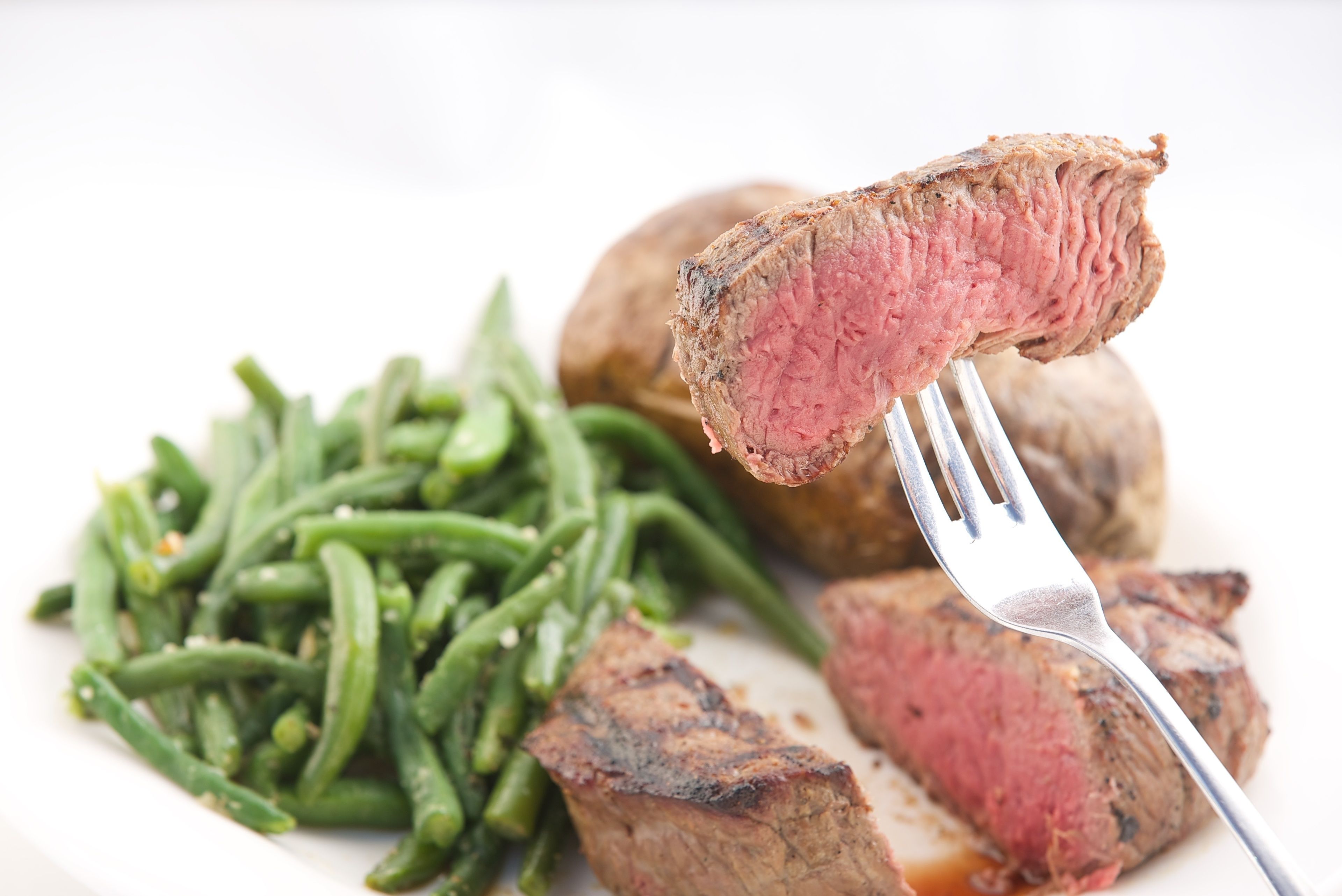 Un plato con un bistec a la parrilla, judías verdes y una papa entera.