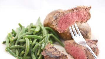 Un plato con un bistec a la parrilla, judías verdes y una papa entera.