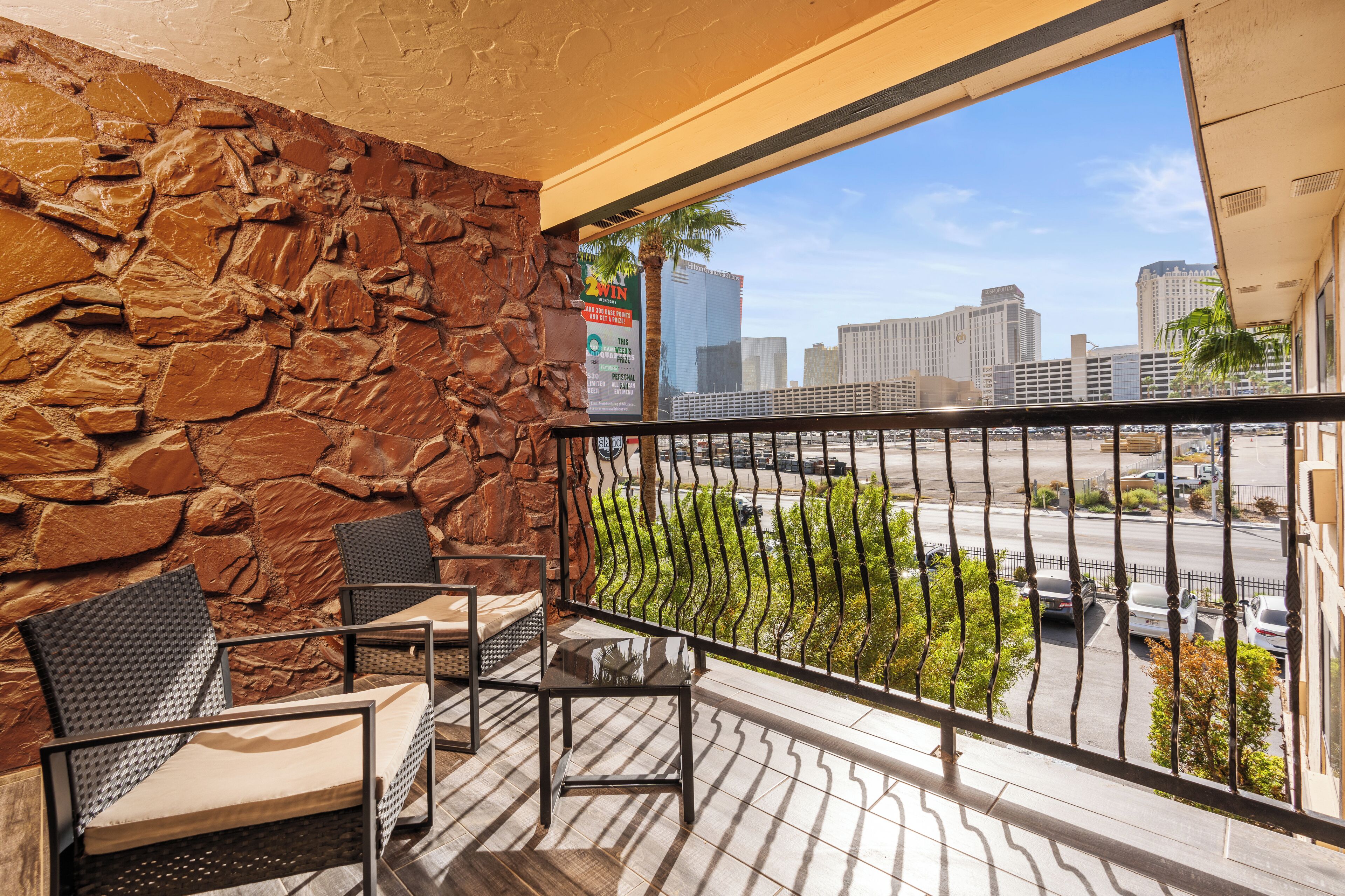 A balcony with stone walls, metal railings, and two wicker chairs.