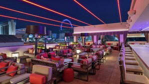 A rooftop bar with multiple seating areas, a view of the city skyline, and a neon light display. - Ellis Island Hotel (Las Vegas)