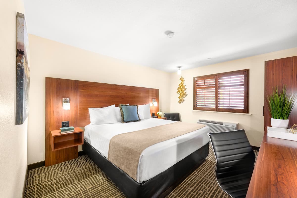 Una habitación de hotel con una cama grande, cabecera de madera, mesitas de noche, un escritorio y una silla.