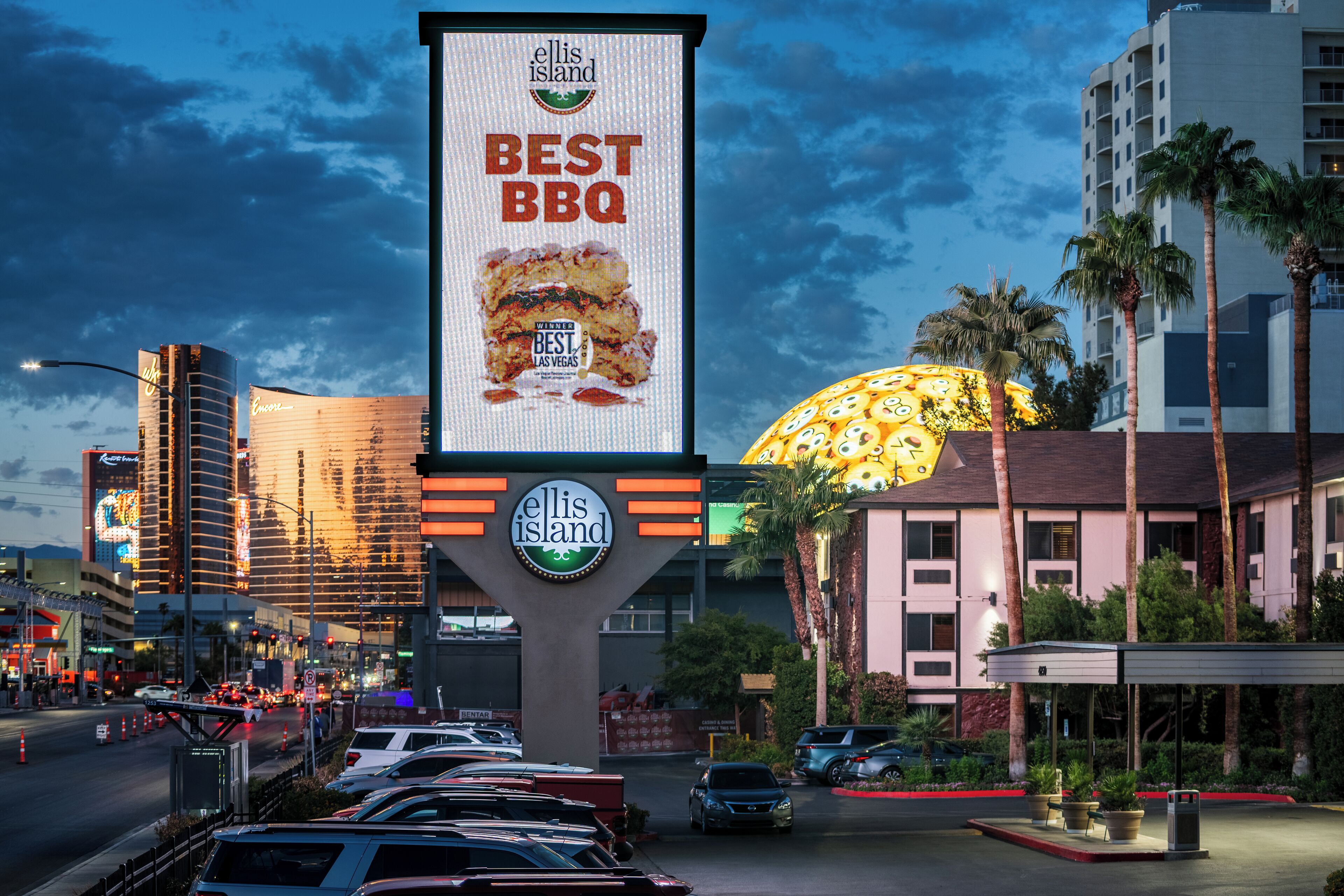 A billboard advertising 'Best BBQ' at Ellis Island, with a large illuminated sign and a building in the background.