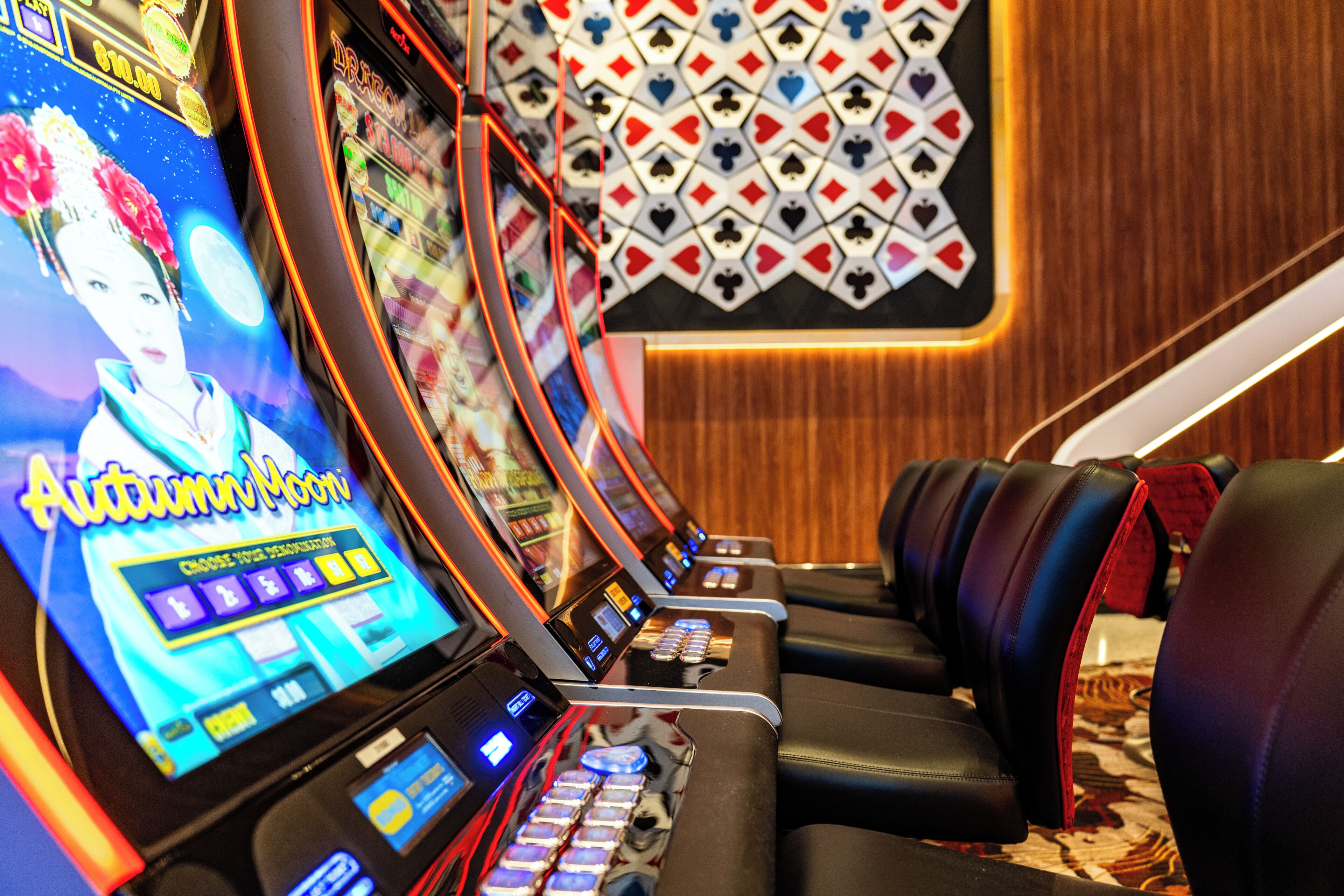 A row of slot machines with a digital display, a patterned wall, and leather seating.